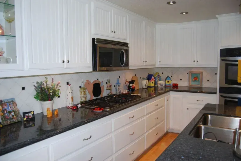A kitchen with white cabinets and black counter tops