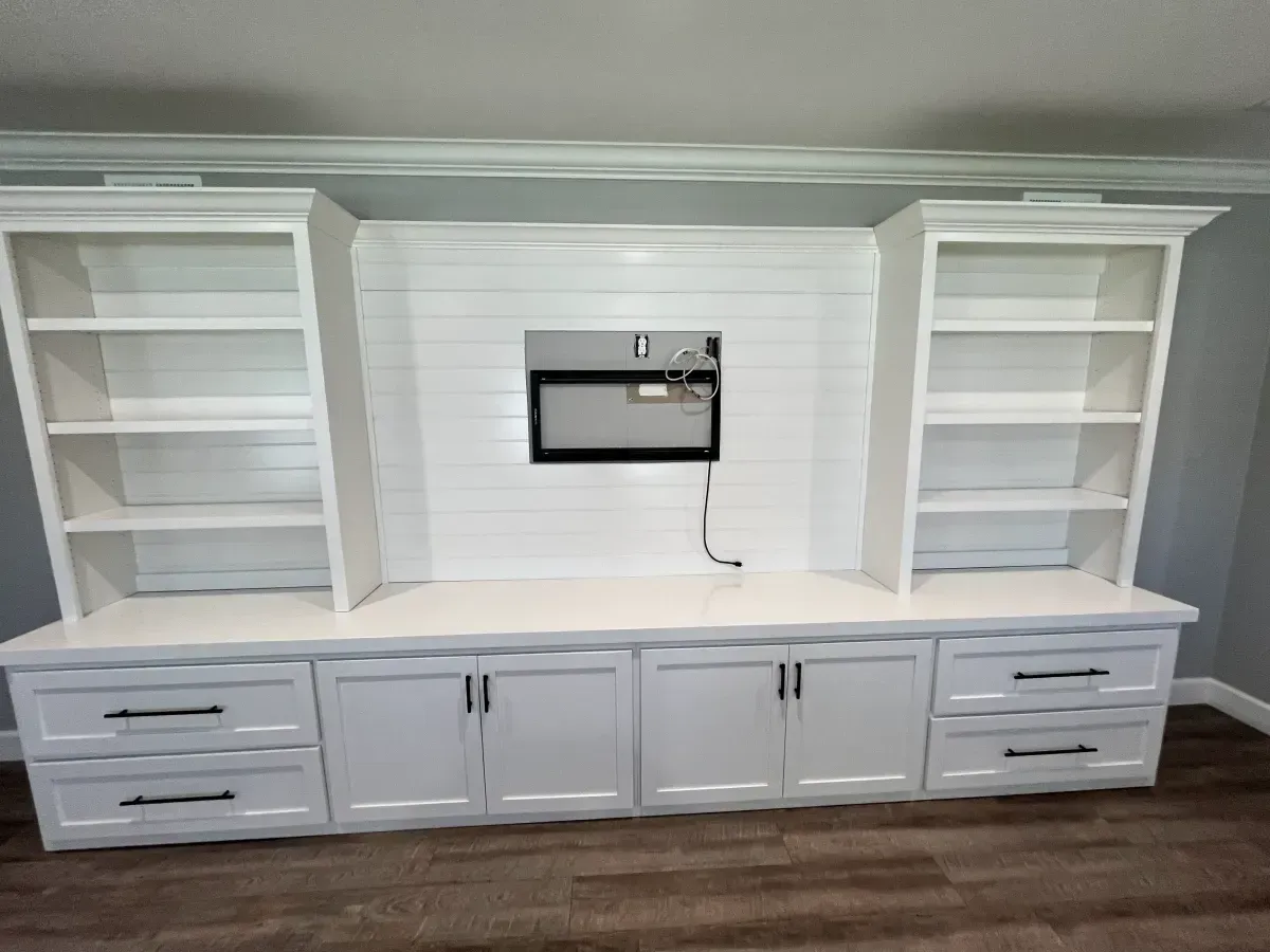 A living room with white cabinets and shelves and a flat screen tv mounted on the wall.