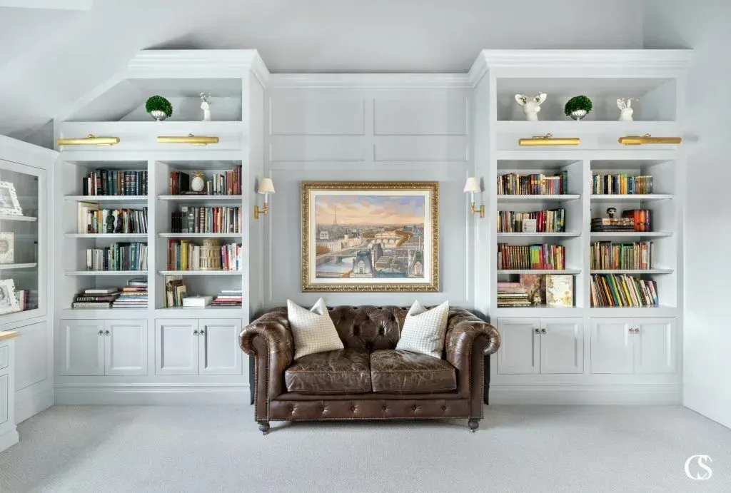 A living room with a brown couch and a painting on the wall.