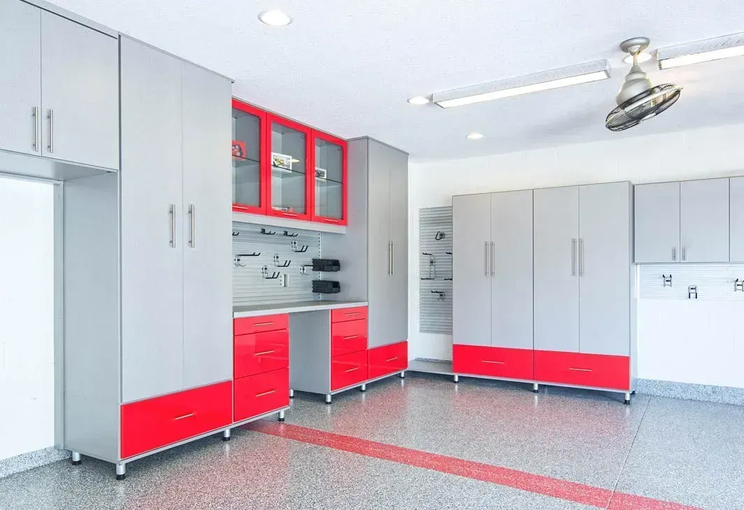 A garage with gray cabinets and red drawers and a ceiling fan.