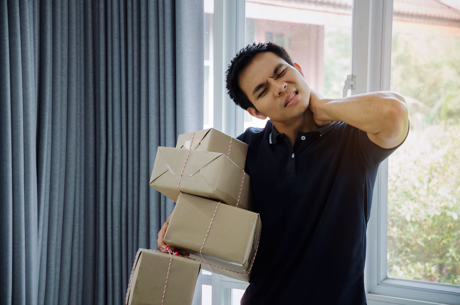 Man holding packages, grimacing with hand on neck, suggesting pain.