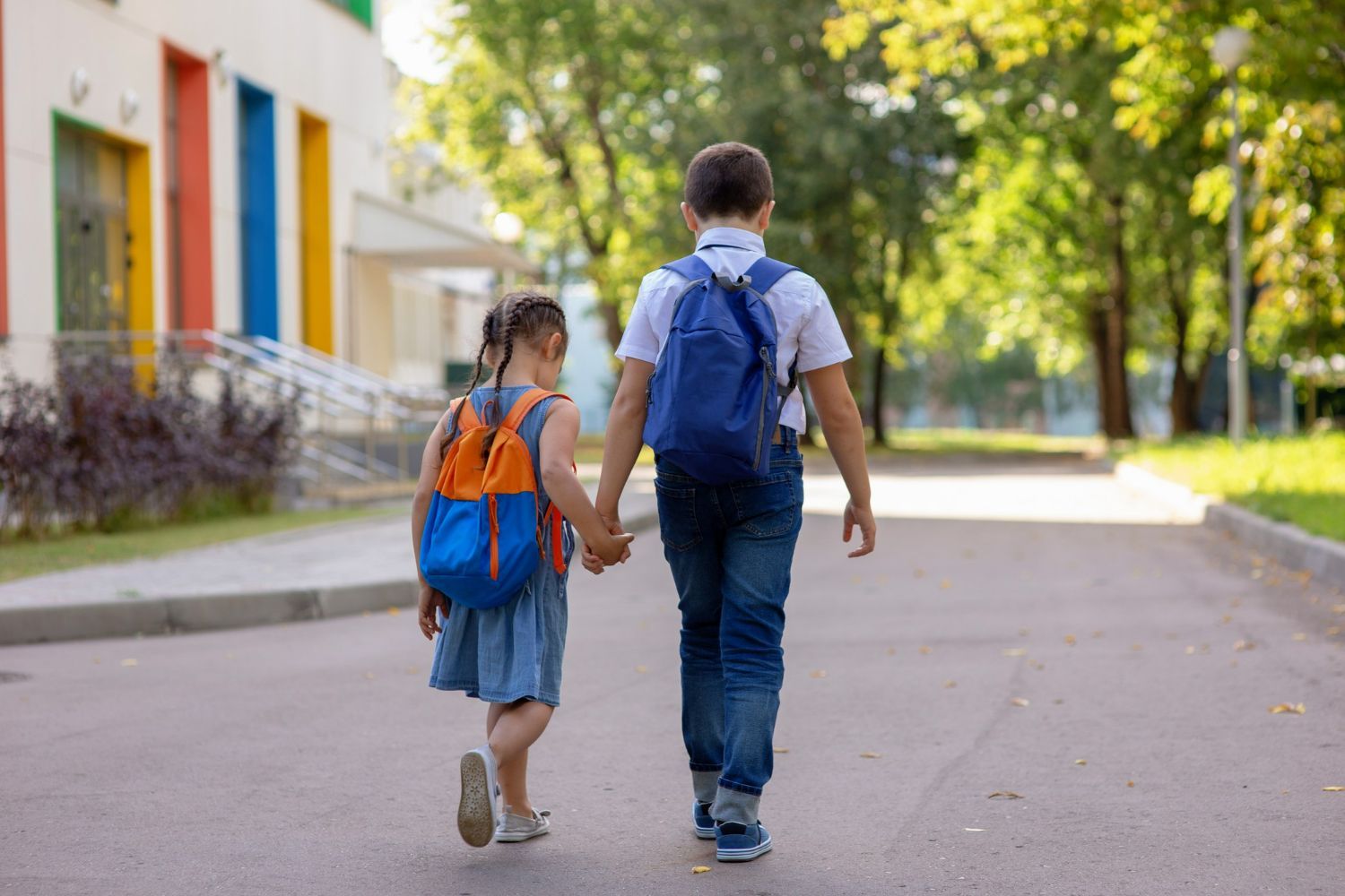 A boy and a girl are walking down the street holding hands.