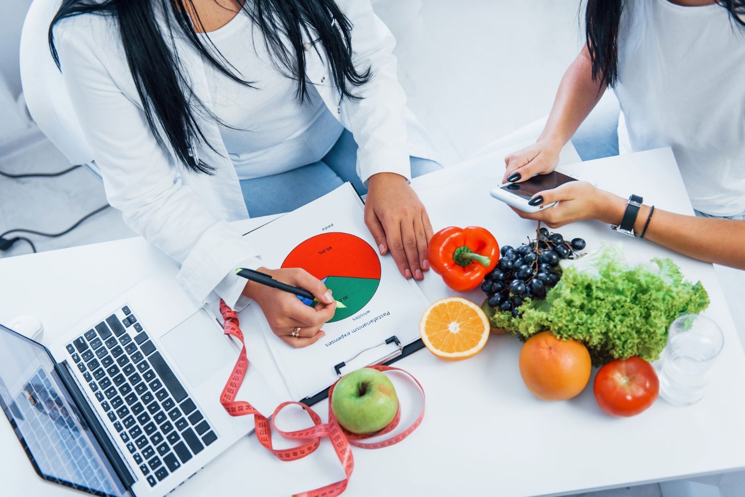 Two people with fruits and pie chart discussing nutrition plan at a table.