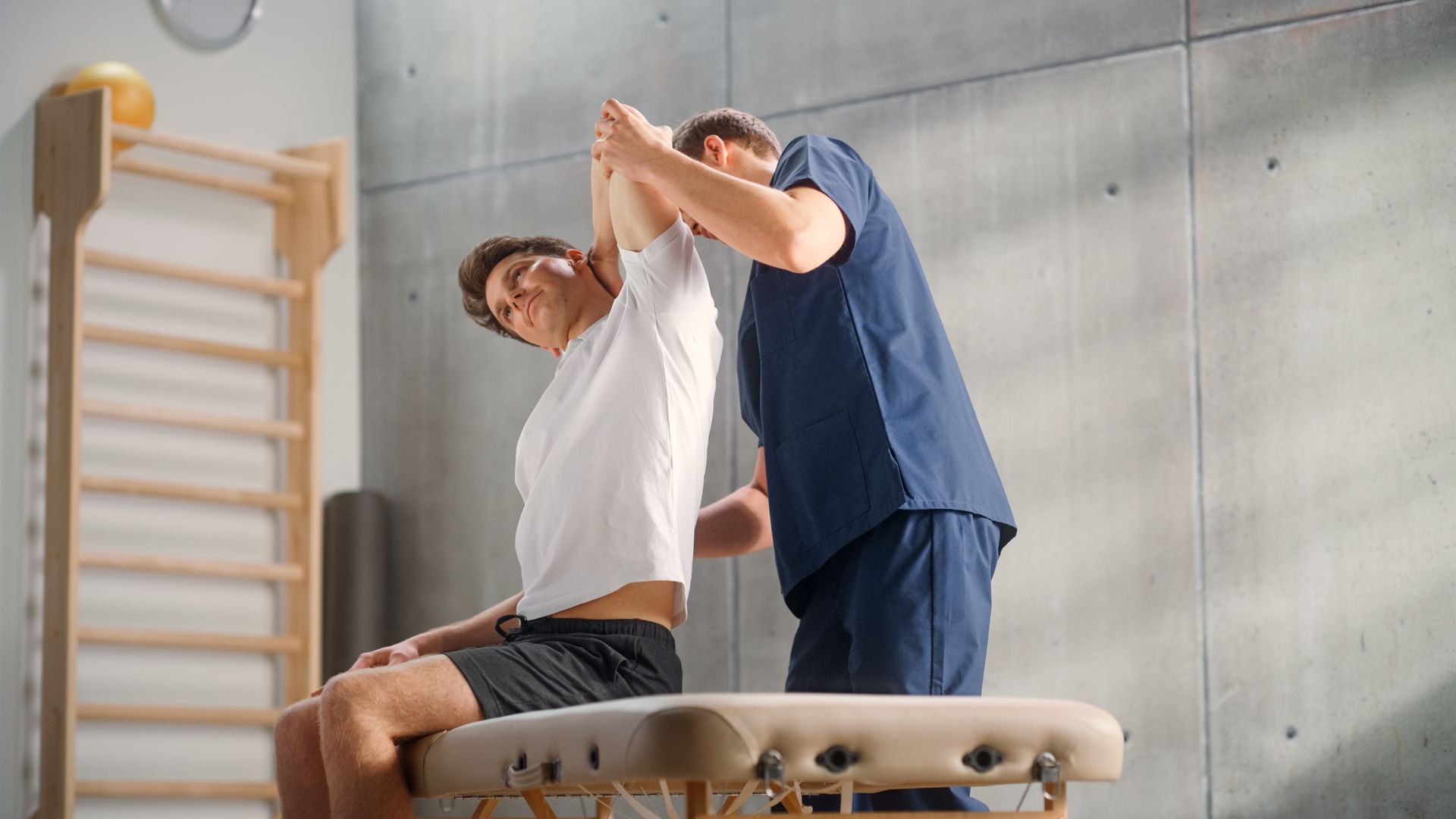 Physiotherapist assisting a seated patient, stretching the arm in a clinic.