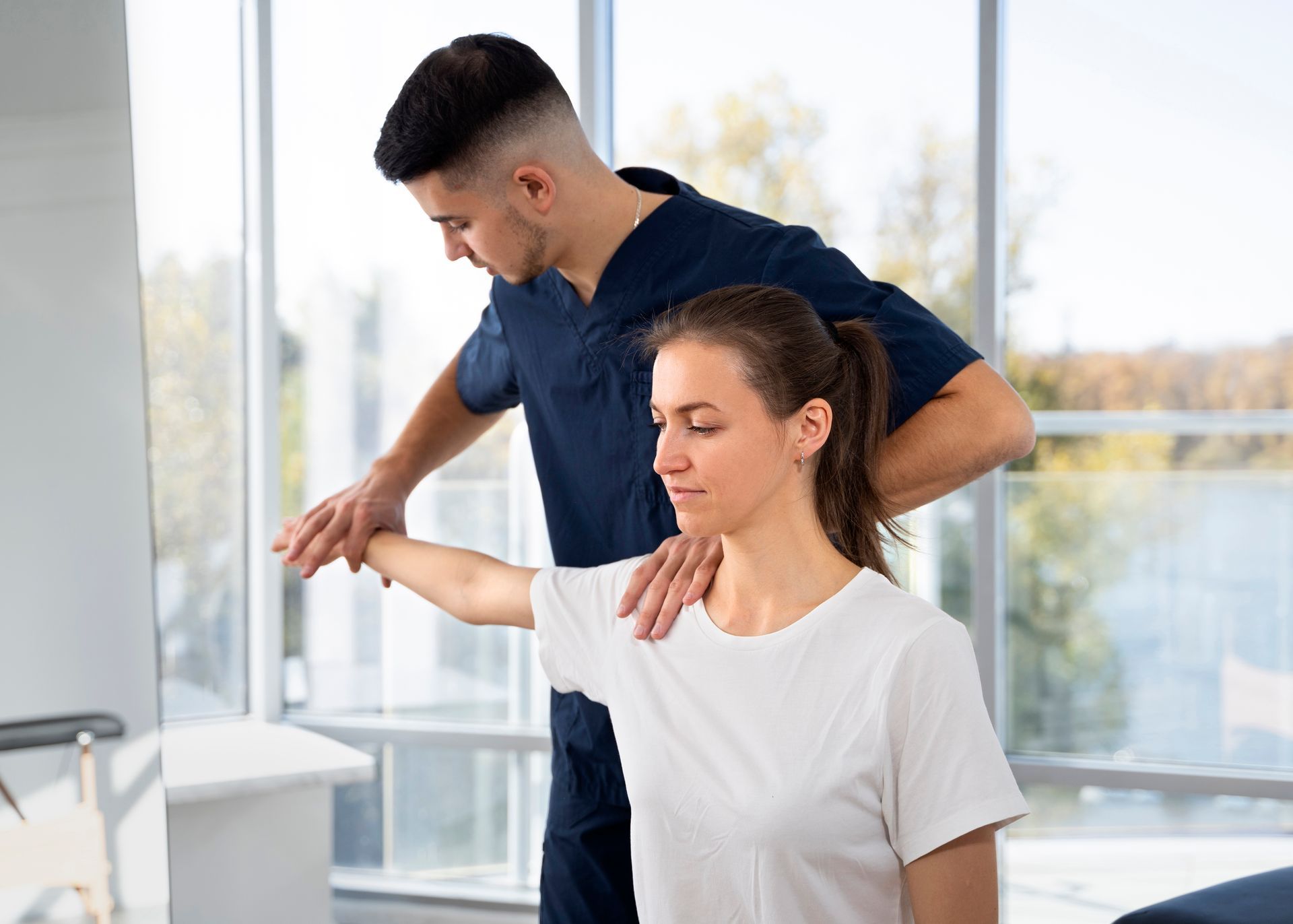 A man is helping a woman stretch her arm in a hospital.