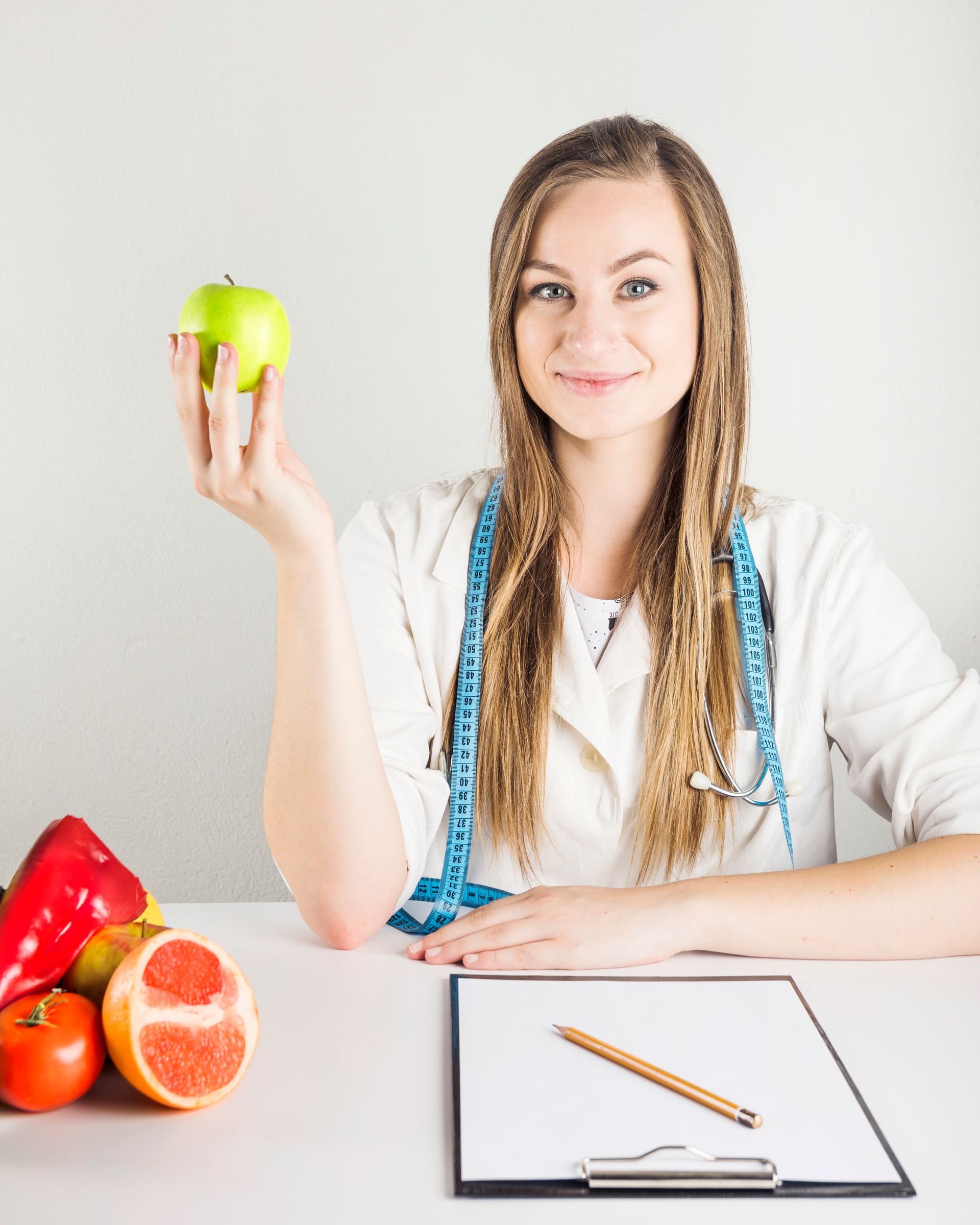 A female dietitian is sitting at a table holding an apple.