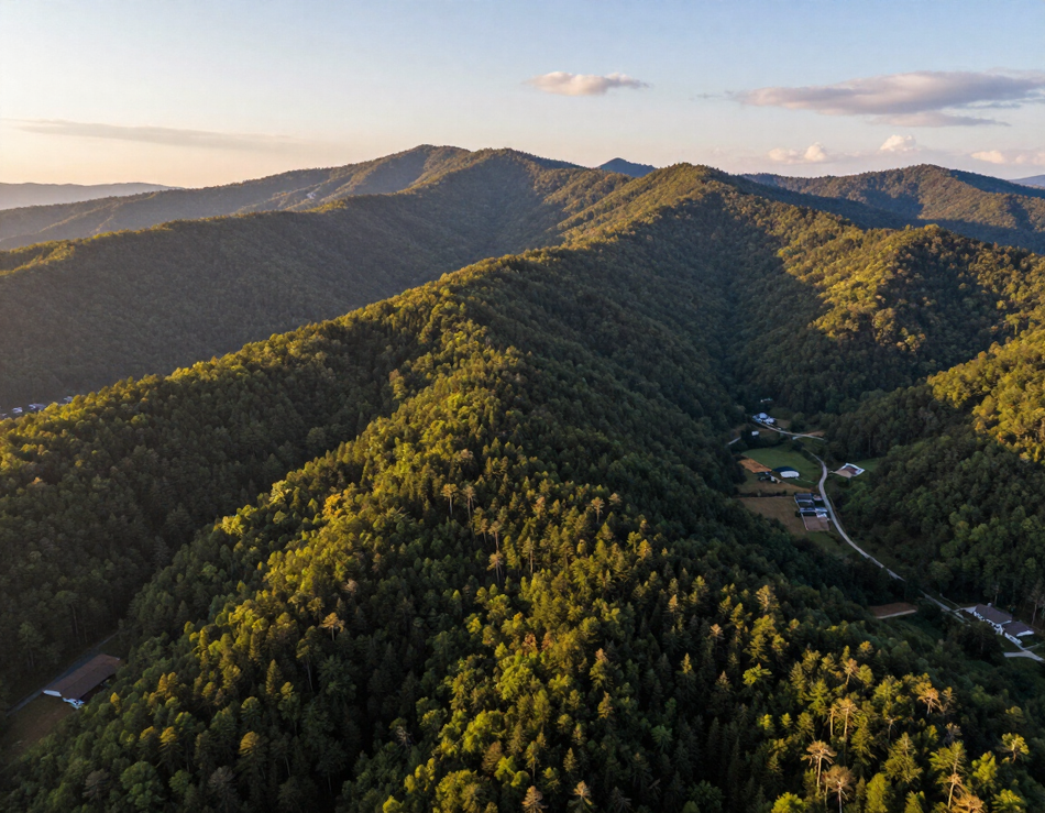 Sunlit forested mountain ridge with a valley and small buildings below at sunset