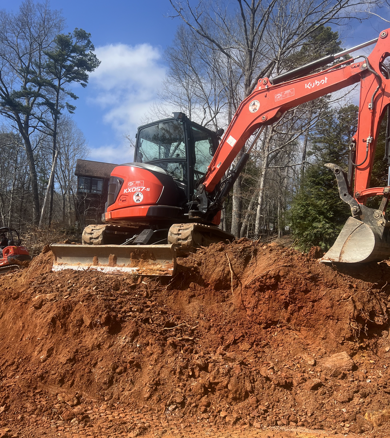 Orange excavator digging in a muddy wooded area under a blue sky
