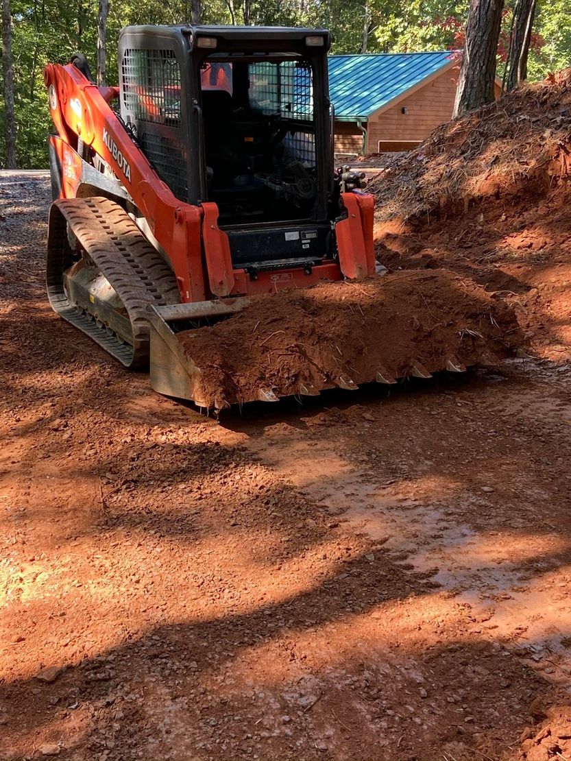 Orange skid-steer bulldozer pushing dirt on a wooded construction site