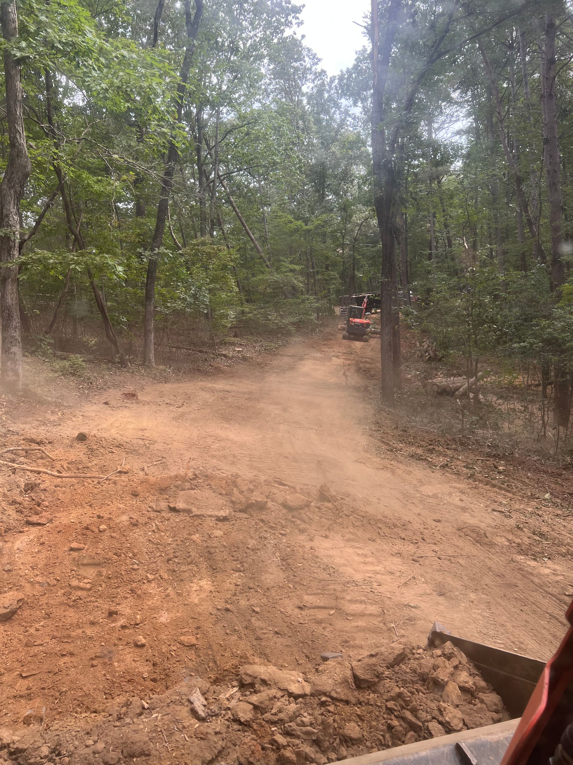 Dusty dirt road through a wooded forest, with an off-road vehicle in the distance.
