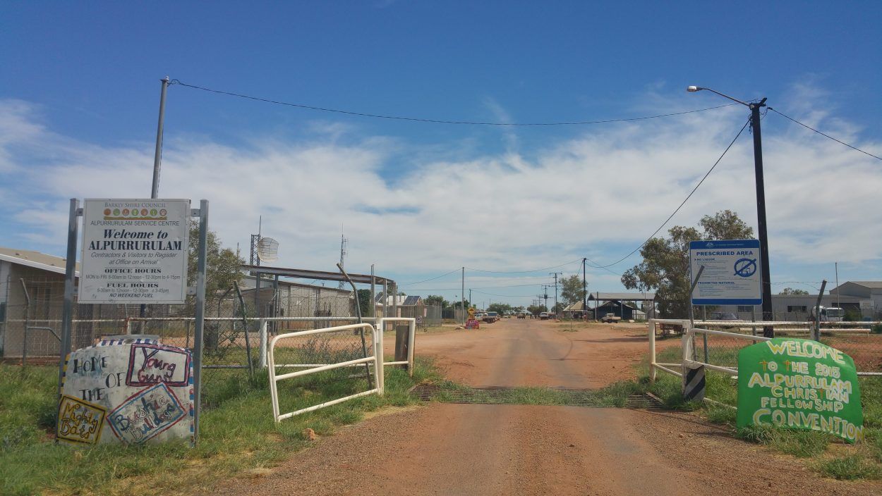A dirt road with a fence and a sign on the side of it.