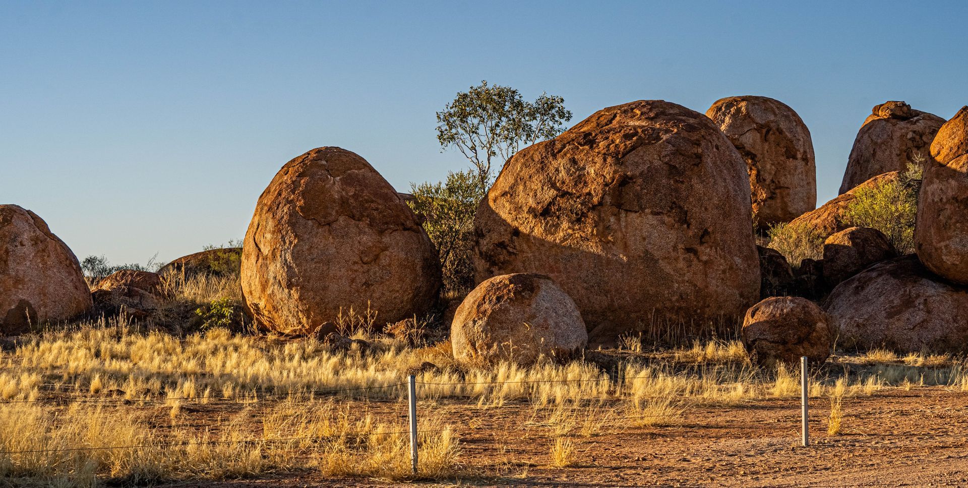 A fence surrounds a large rock formation in the desert.