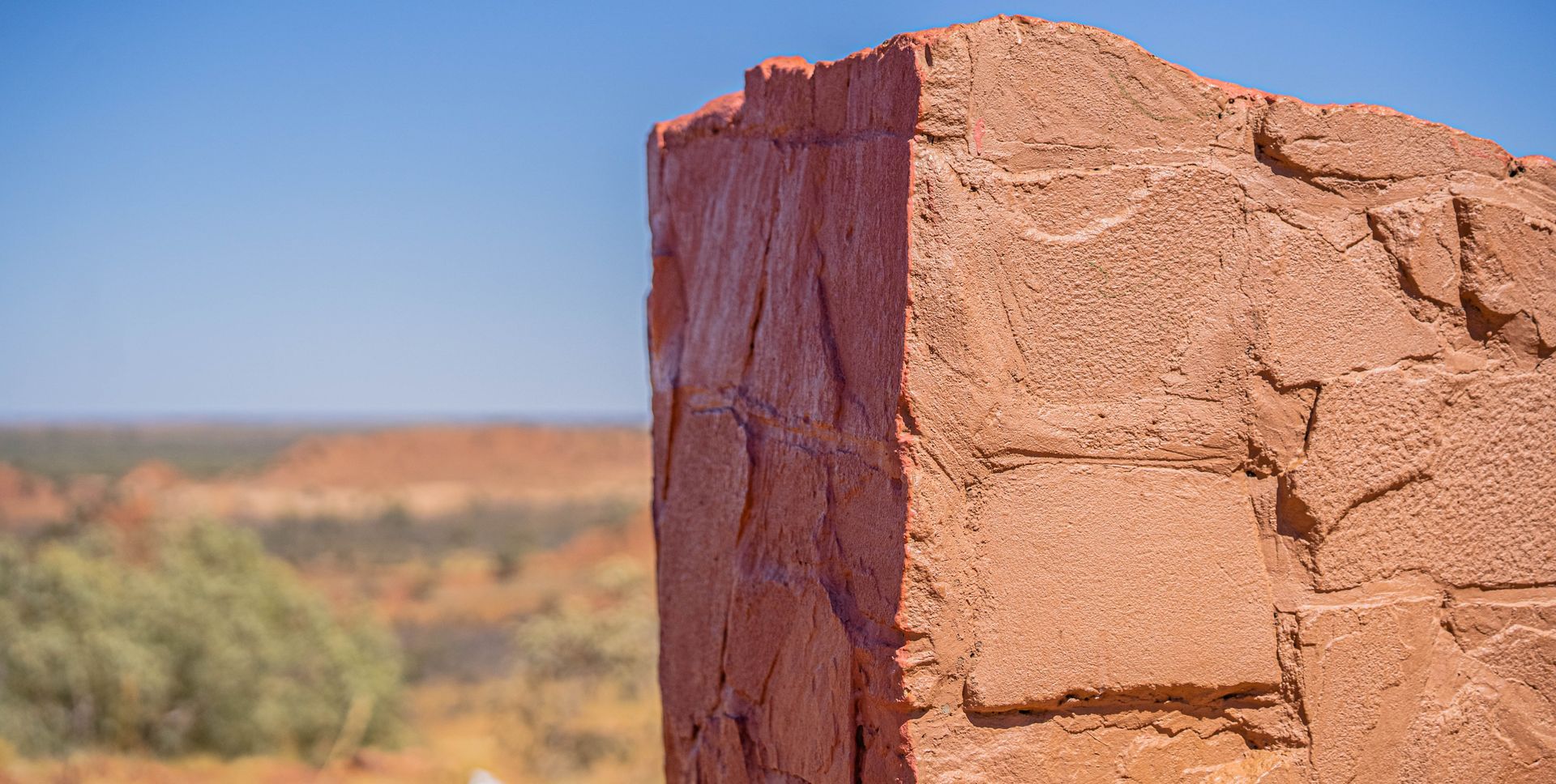 A close up of a red rock in the desert with a blue sky in the background.