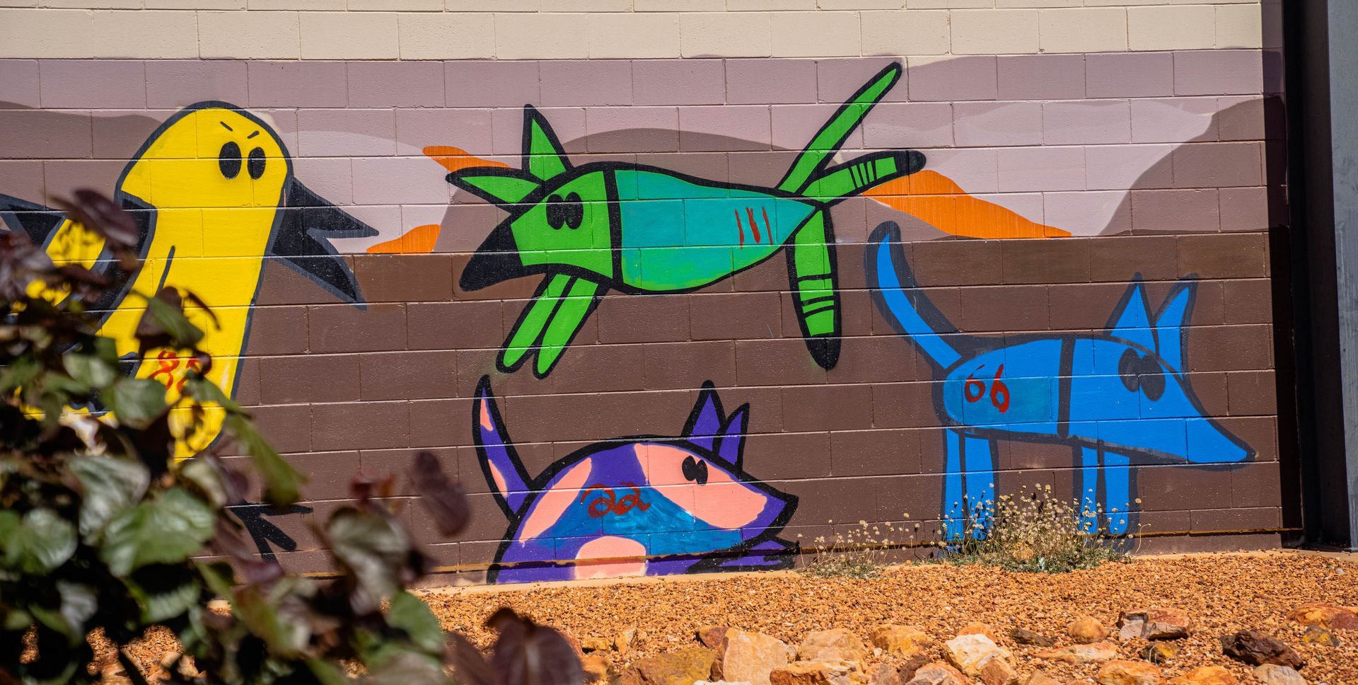 A mural of a bird , a dog , and a plane on a brick wall.