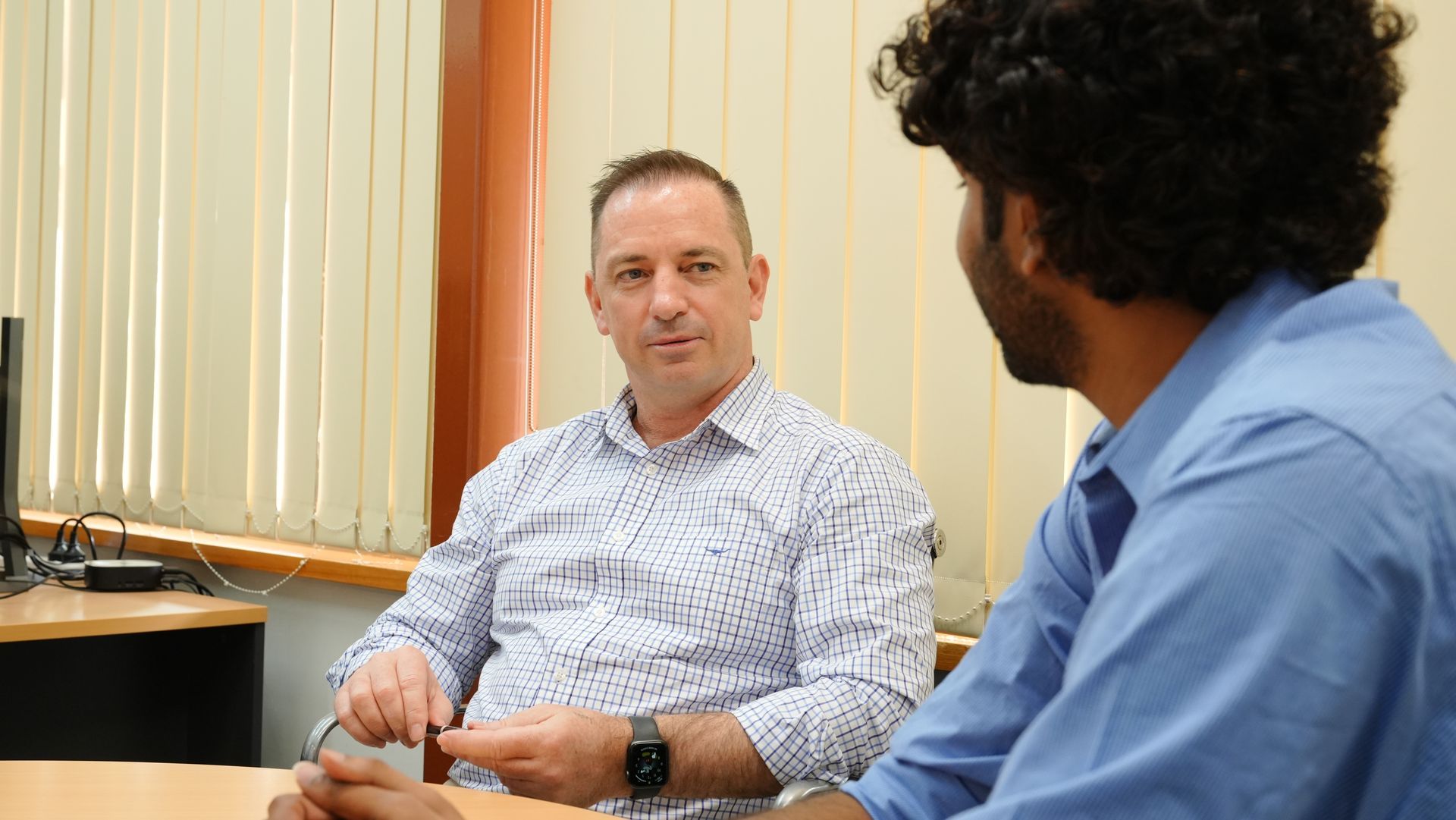 Two men are sitting at a table talking to each other.