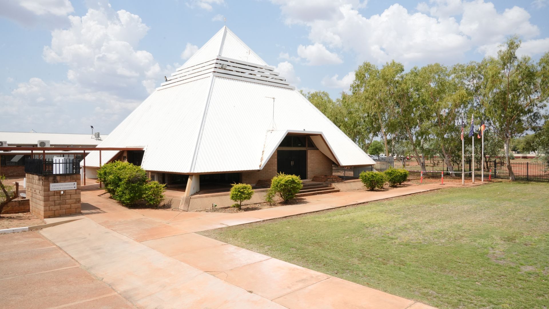A large white pyramid shaped building is surrounded by grass and trees.