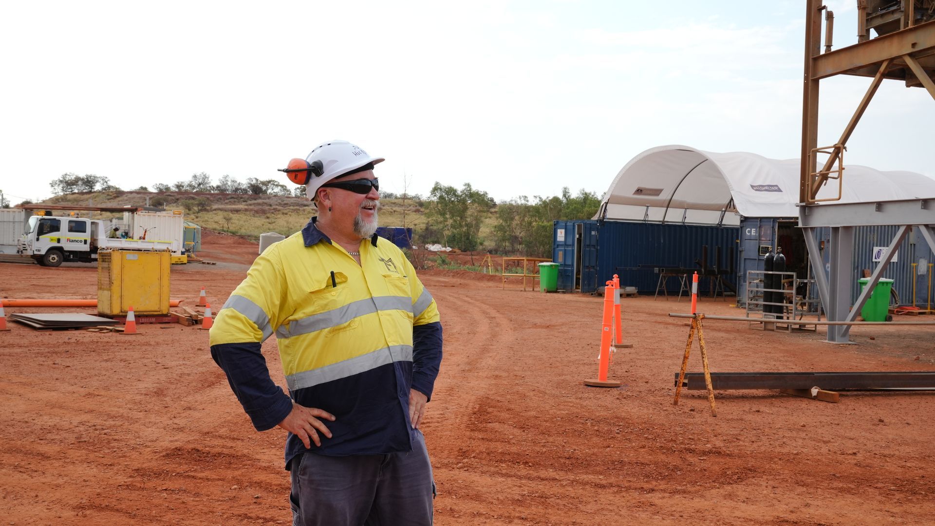 A man wearing a hard hat and safety vest is standing in a dirt field.
