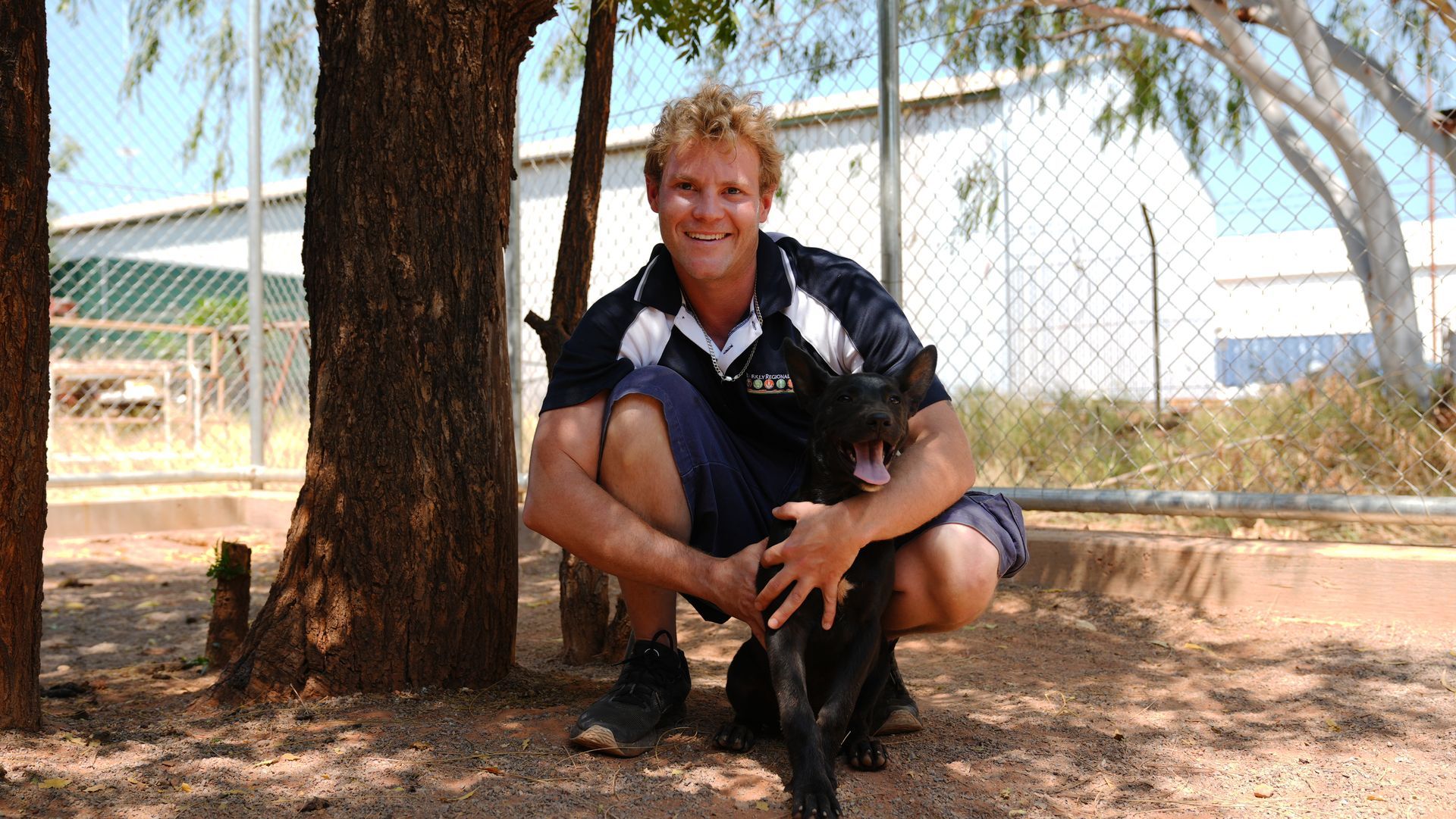 A man kneeling down next to a tree with a dog