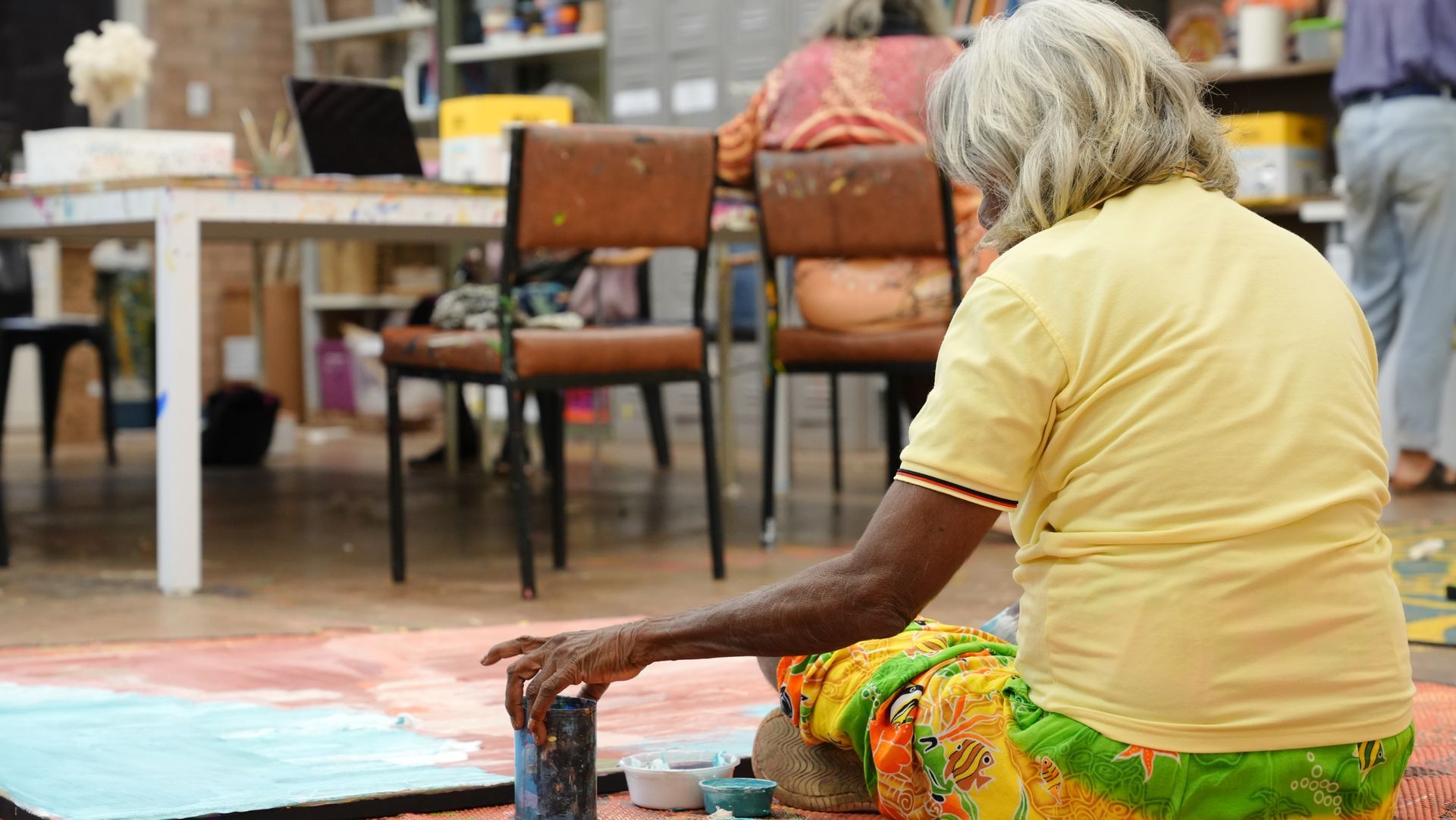 A woman is sitting on the floor painting a picture.