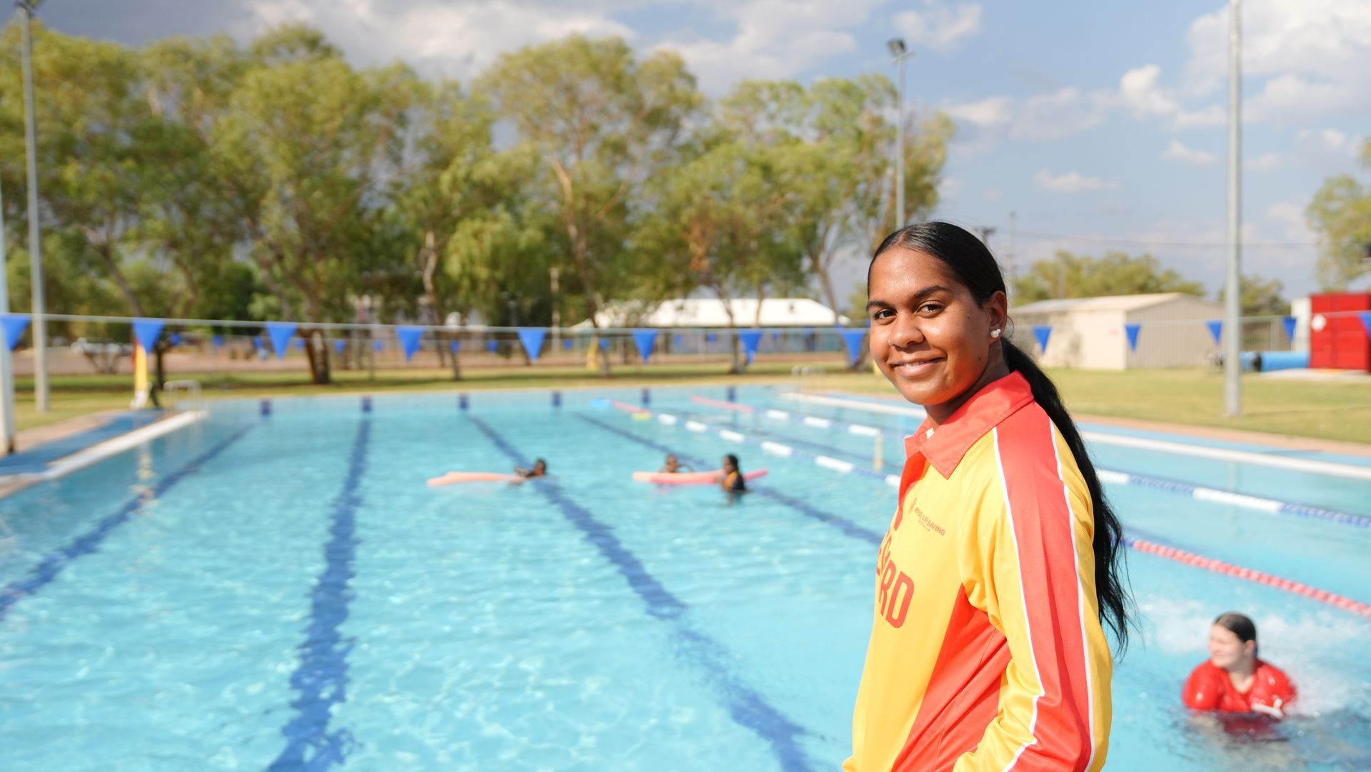 A lifeguard is standing in front of a swimming pool.