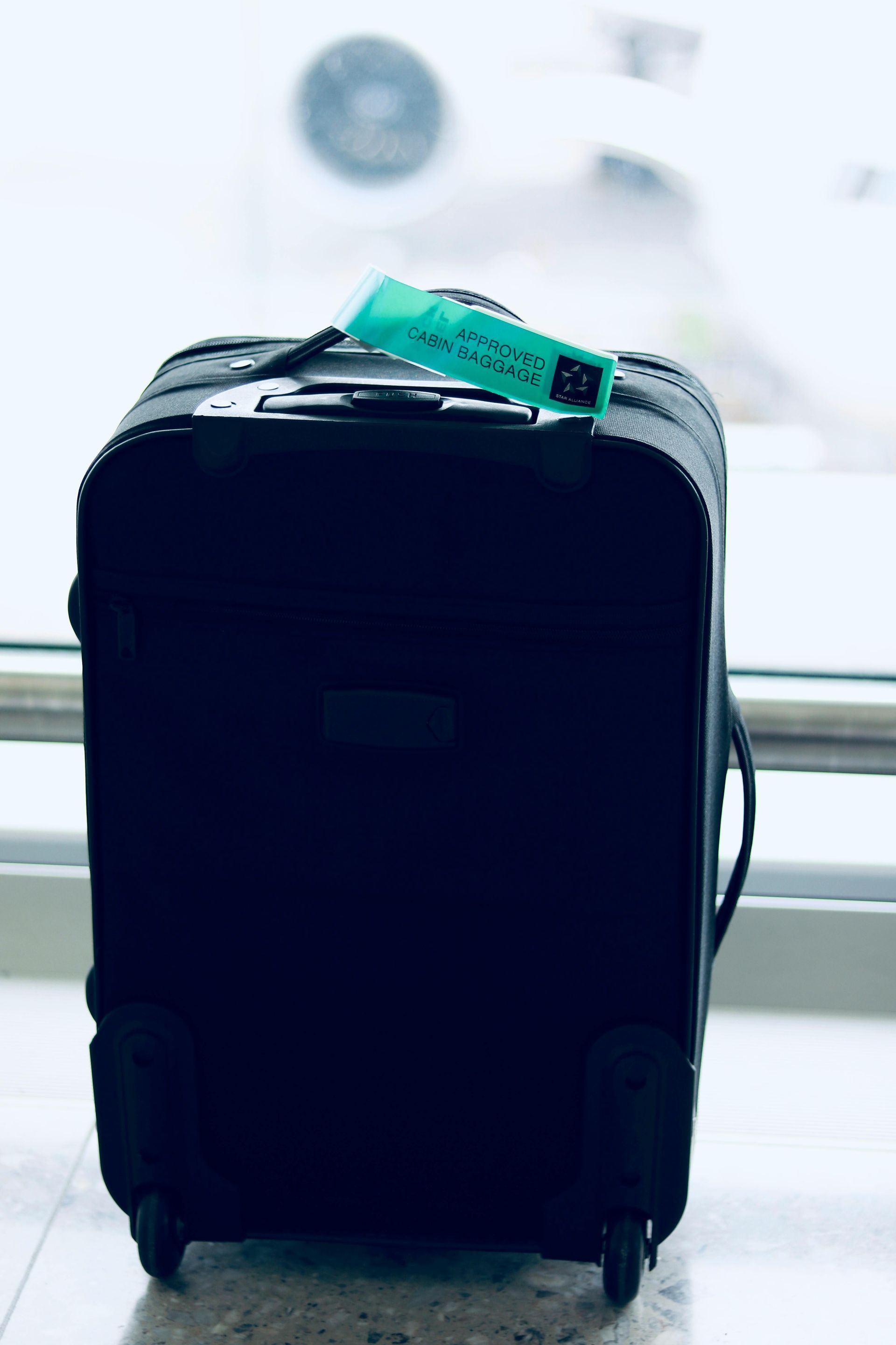 A black suitcase with a blue tag on it is sitting on the floor.