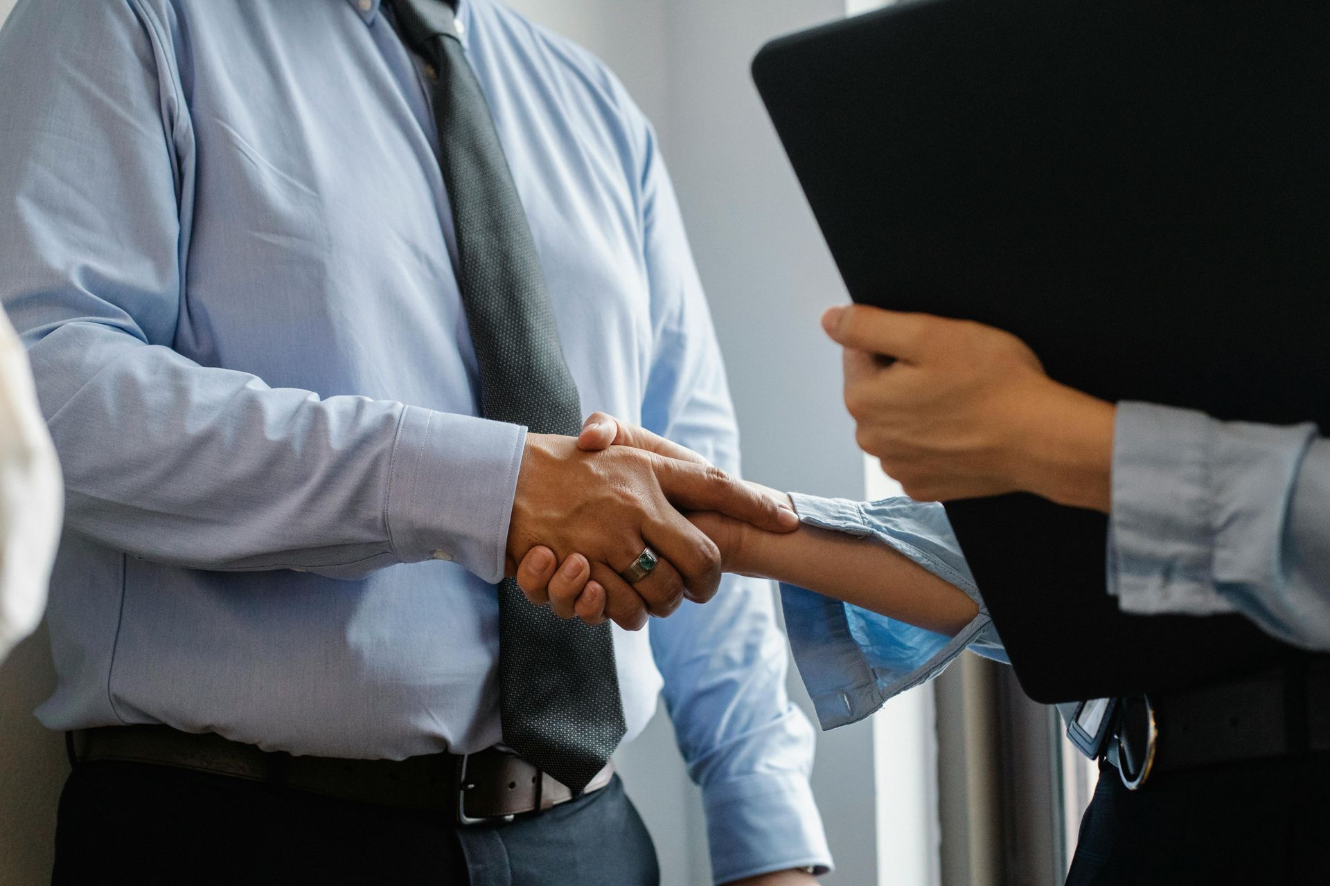 Two people shaking hands over a table; one man and one woman in suits, near a 
