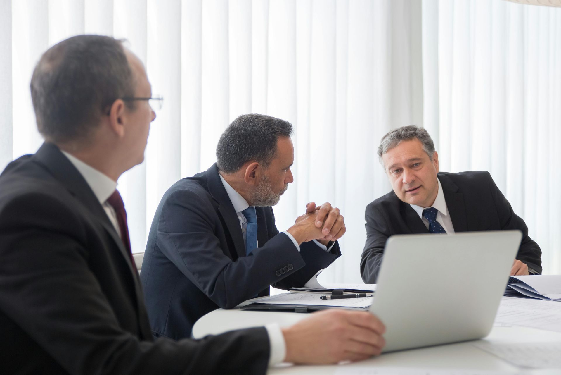 Four businesspeople at a table, one handing a blue folder labeled 