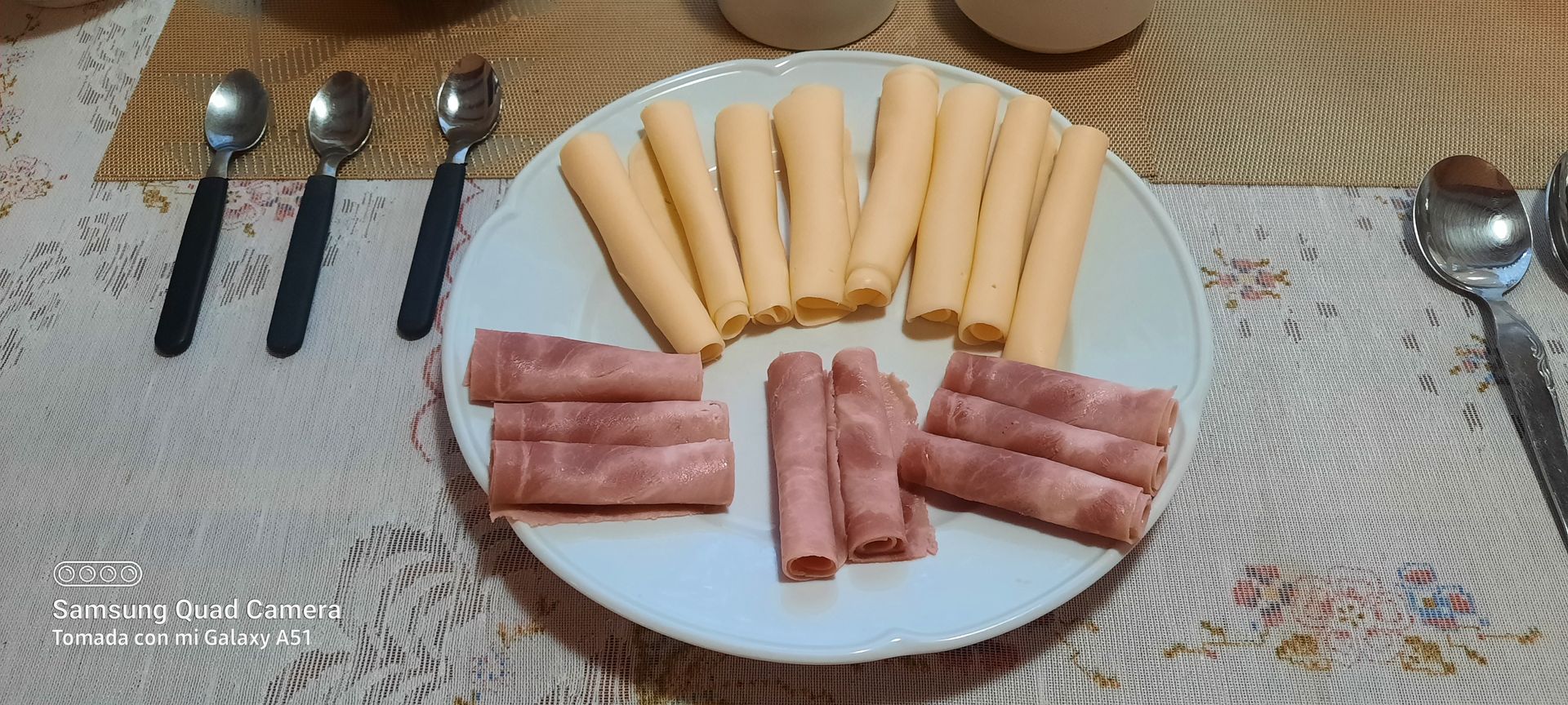 A white plate topped with ham , cheese sticks and spoons on a table.