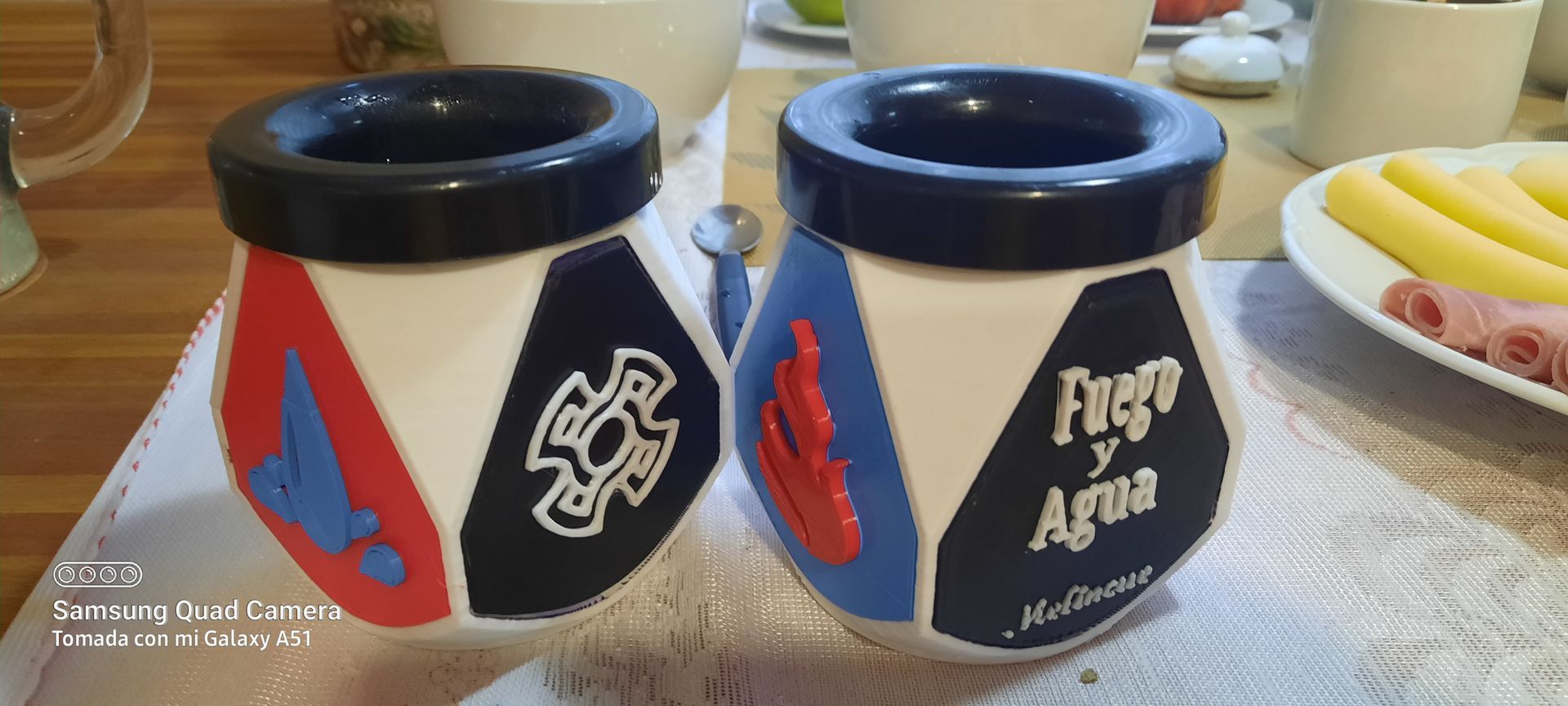 Two cups are sitting on a table next to a plate of food.