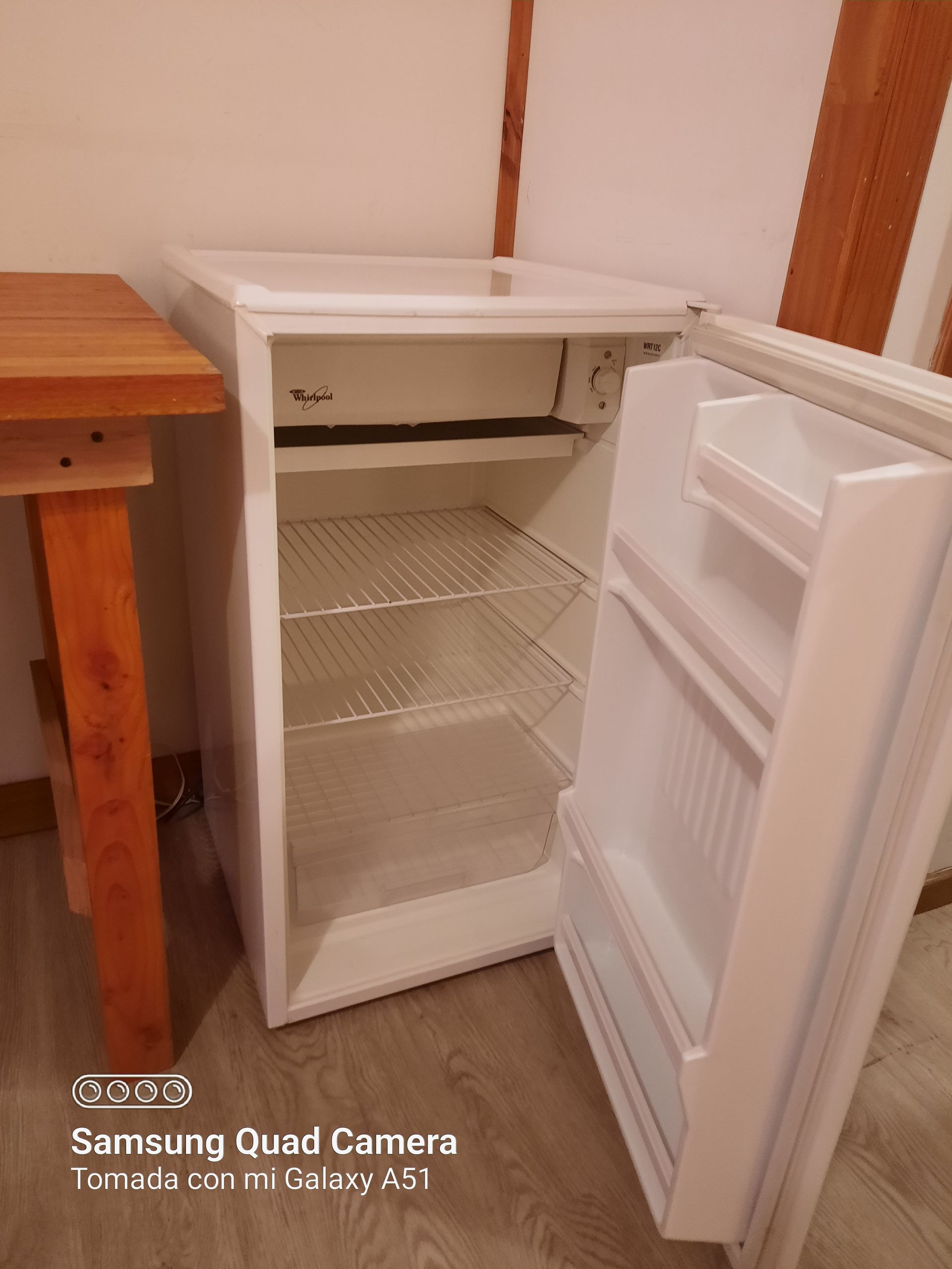 A small white refrigerator with the door open and a wooden table in the background.