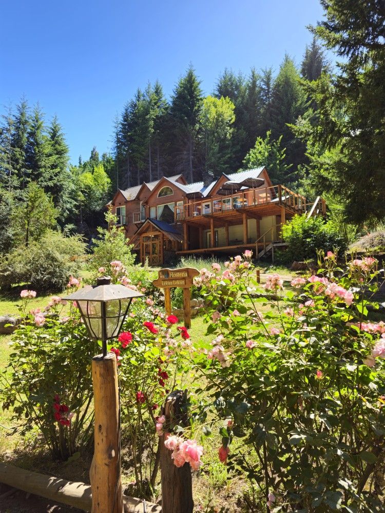 A large wooden house is surrounded by trees and flowers