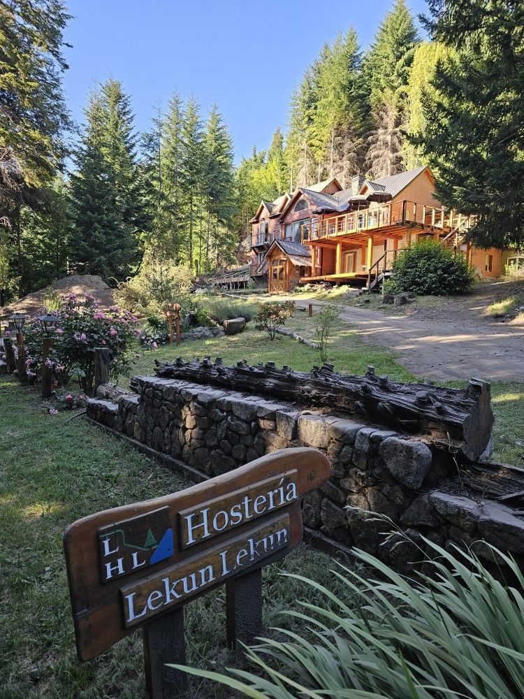 A wooden sign in front of a large house in the woods.