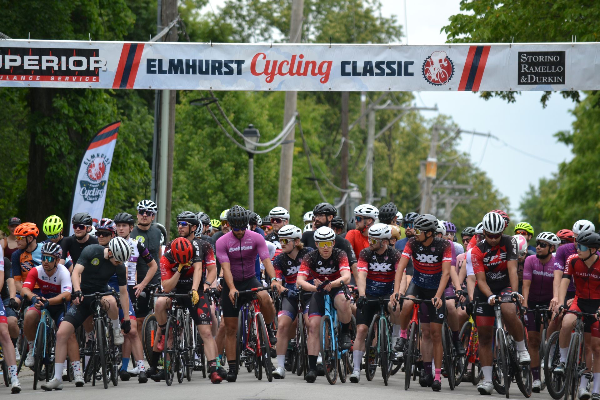 A group of people are riding bicycles in front of a banner that says elmhurst cycling classic