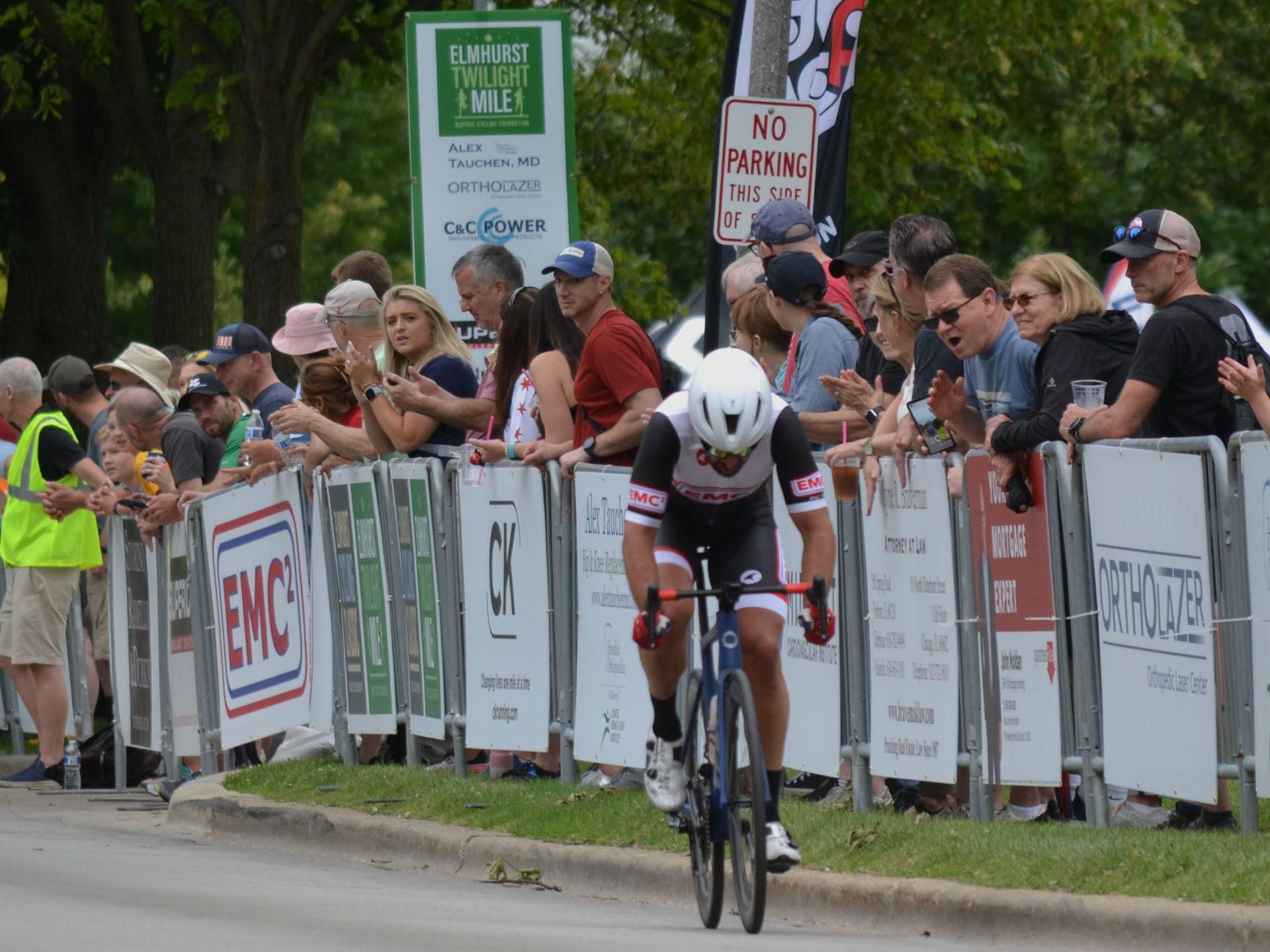 A man riding a bike in front of a crowd with a sign that says no parking