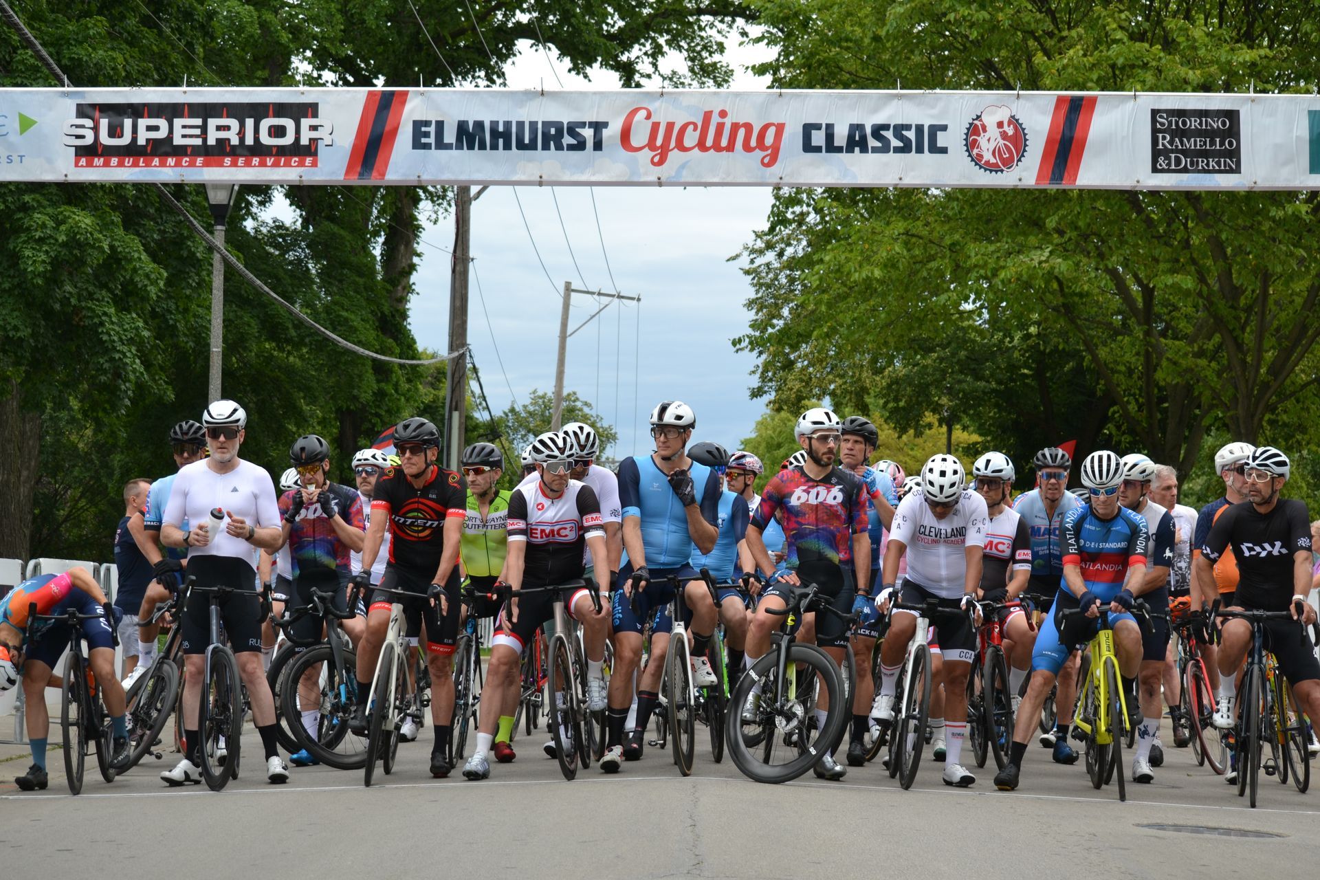 A group of people are riding bicycles in front of a sign that says superior elmhurst cycling classic.