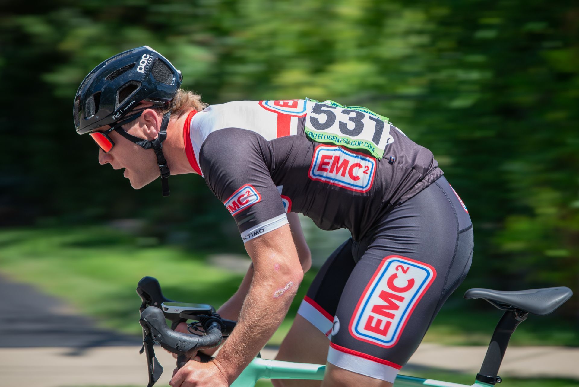 A man wearing a helmet and sunglasses is riding a bike on a road.