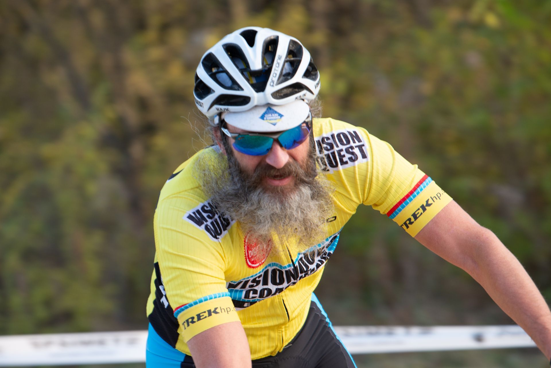 A man with a beard wearing a helmet and sunglasses is riding a bike.