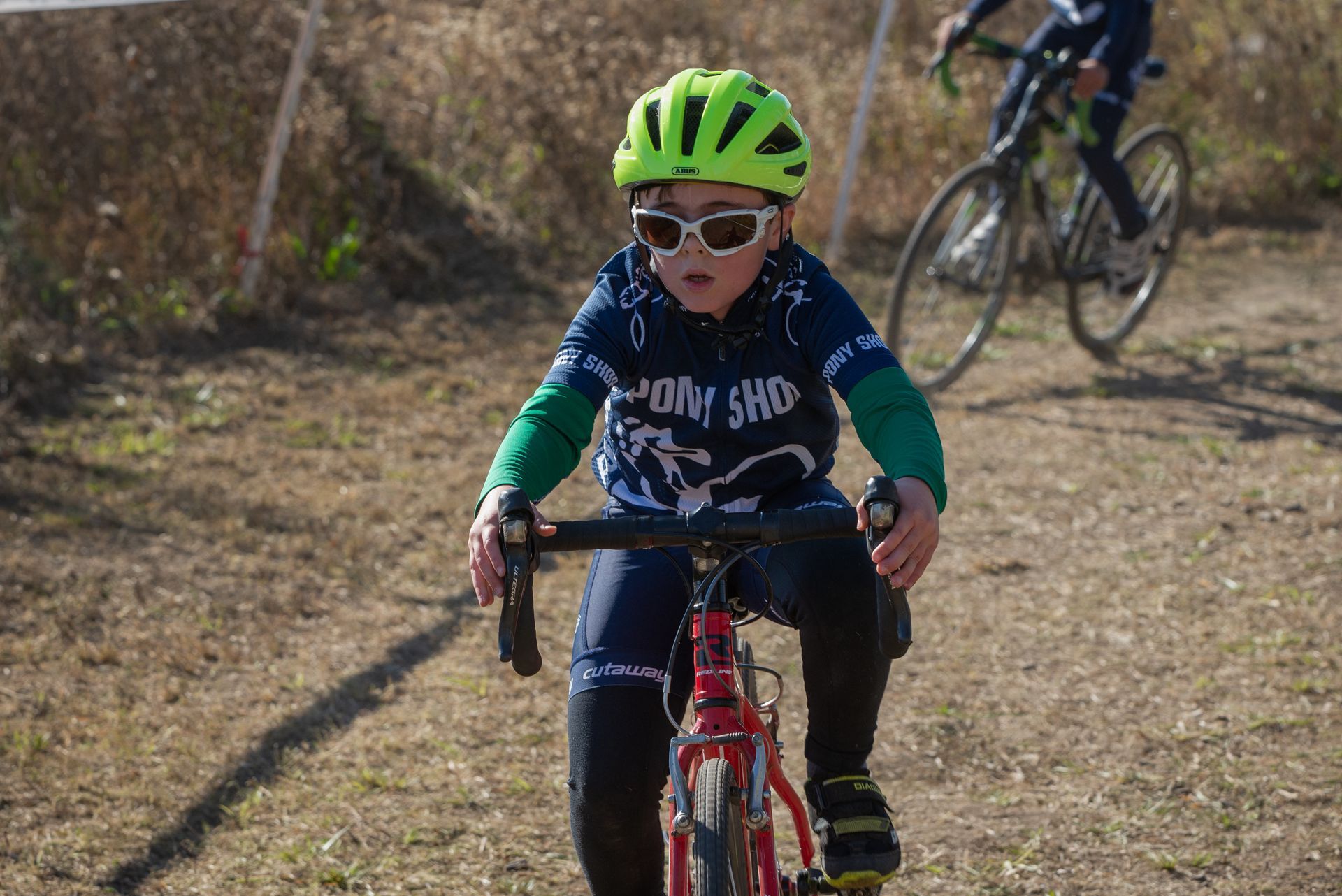 A young boy wearing a helmet and sunglasses is riding a bike on a dirt road.