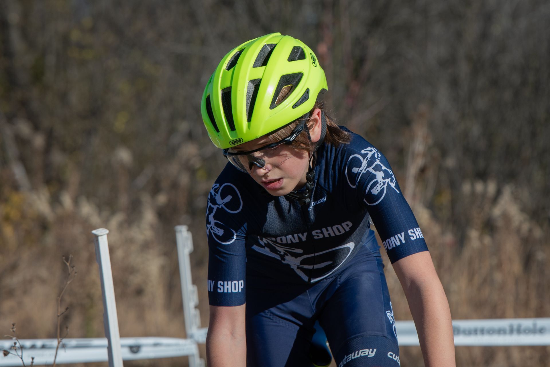 A young girl wearing a yellow helmet and sunglasses is riding a bike.