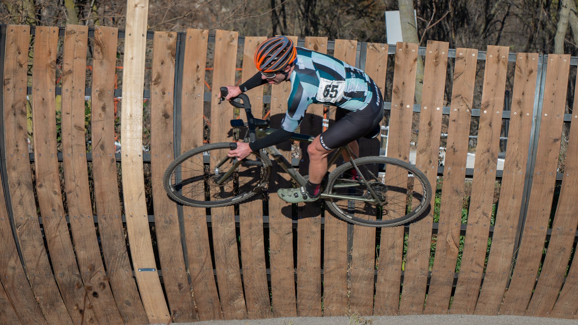 A person is riding a bike over a wooden fence.