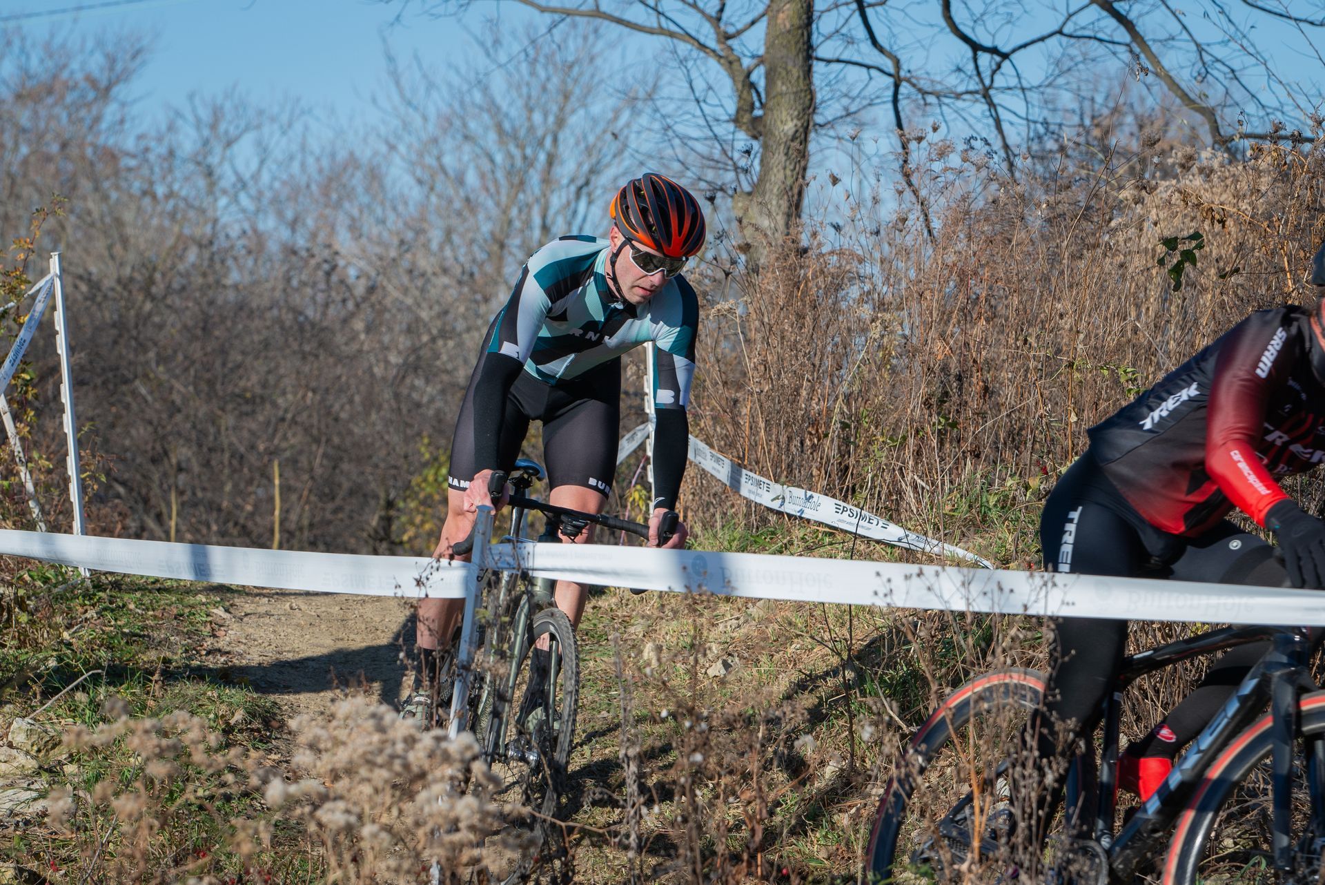 A man is riding a bike on a dirt road next to a fence.