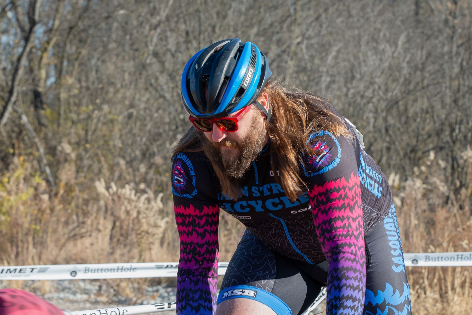 A man with long hair and a beard is wearing a helmet and sunglasses while riding a bike.