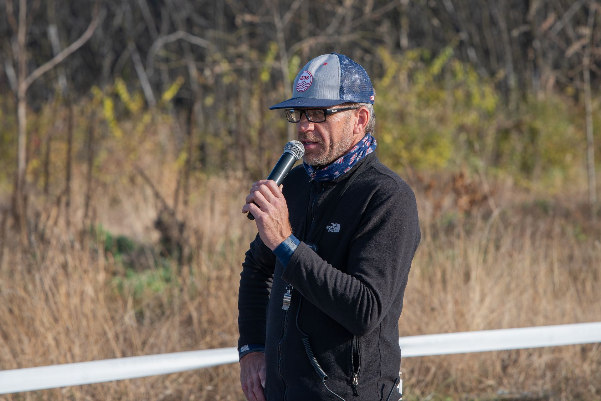 A man is standing in a field holding a microphone.