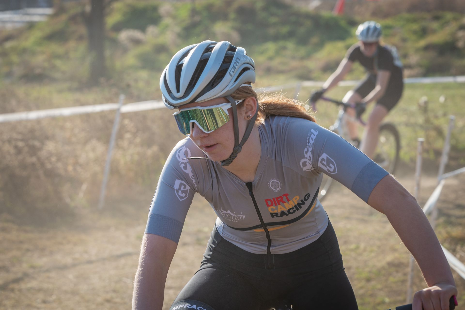 A woman wearing a helmet and sunglasses is riding a bike on a dirt road.