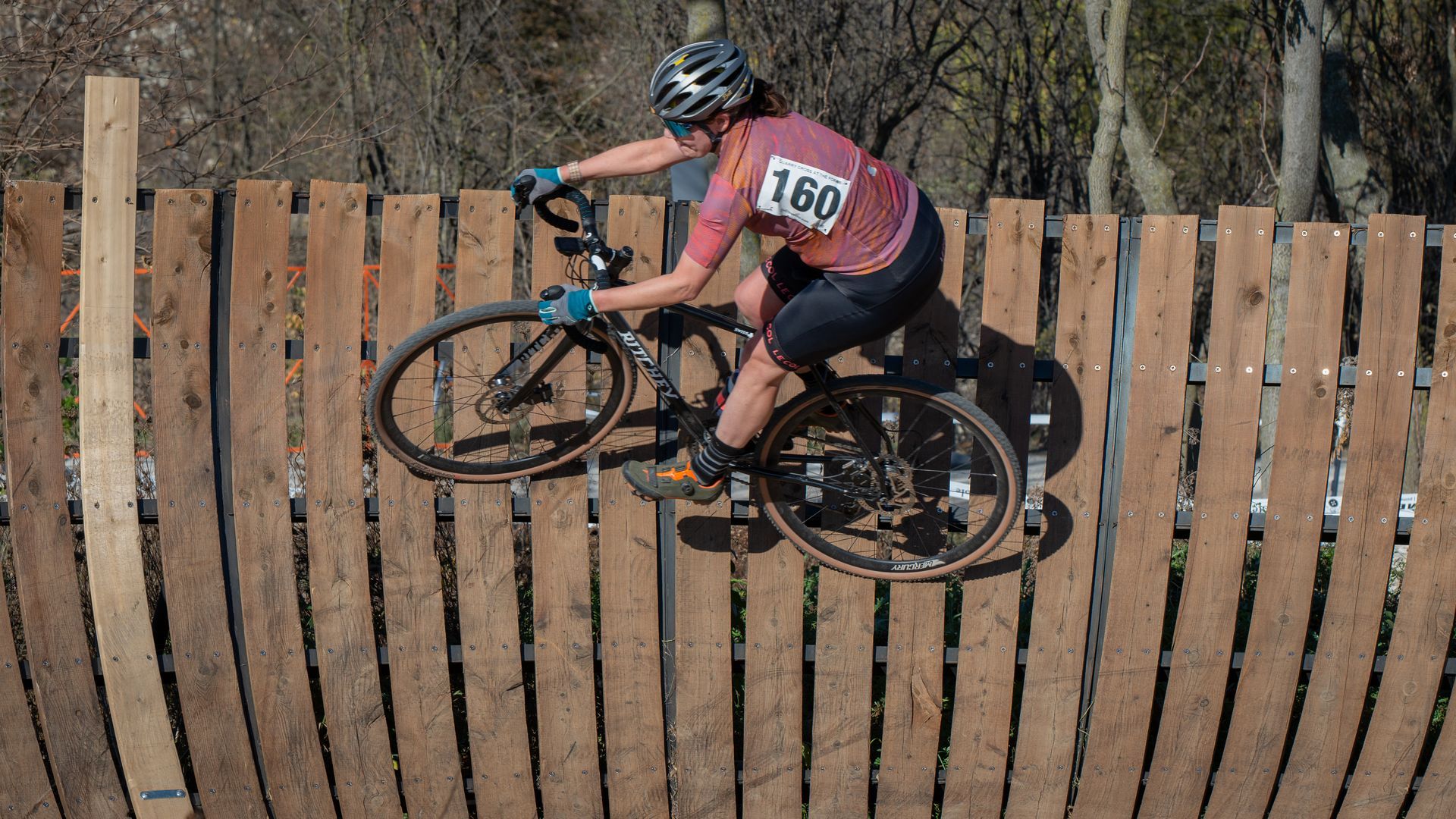 A person is riding a bike over a wooden fence.