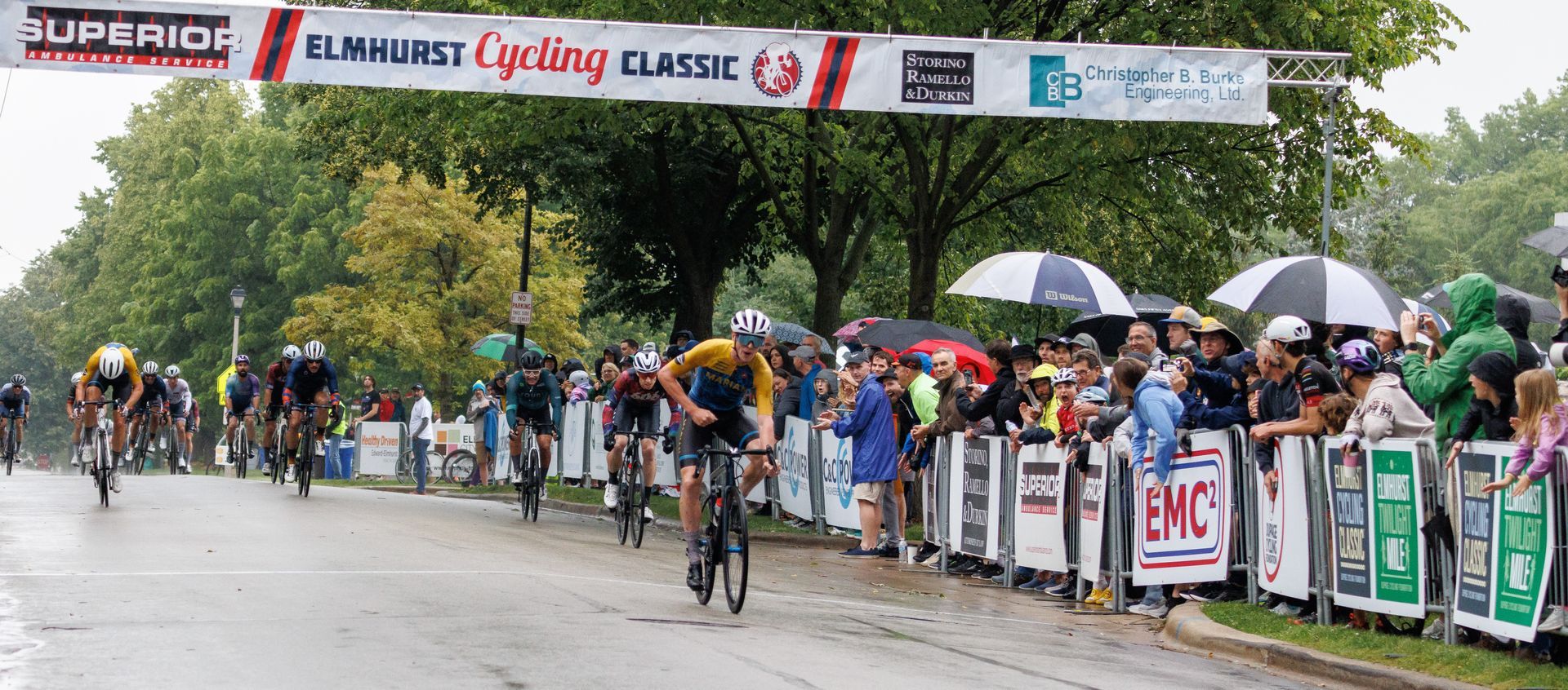 A group of people are riding bikes down a road under a banner that says superior