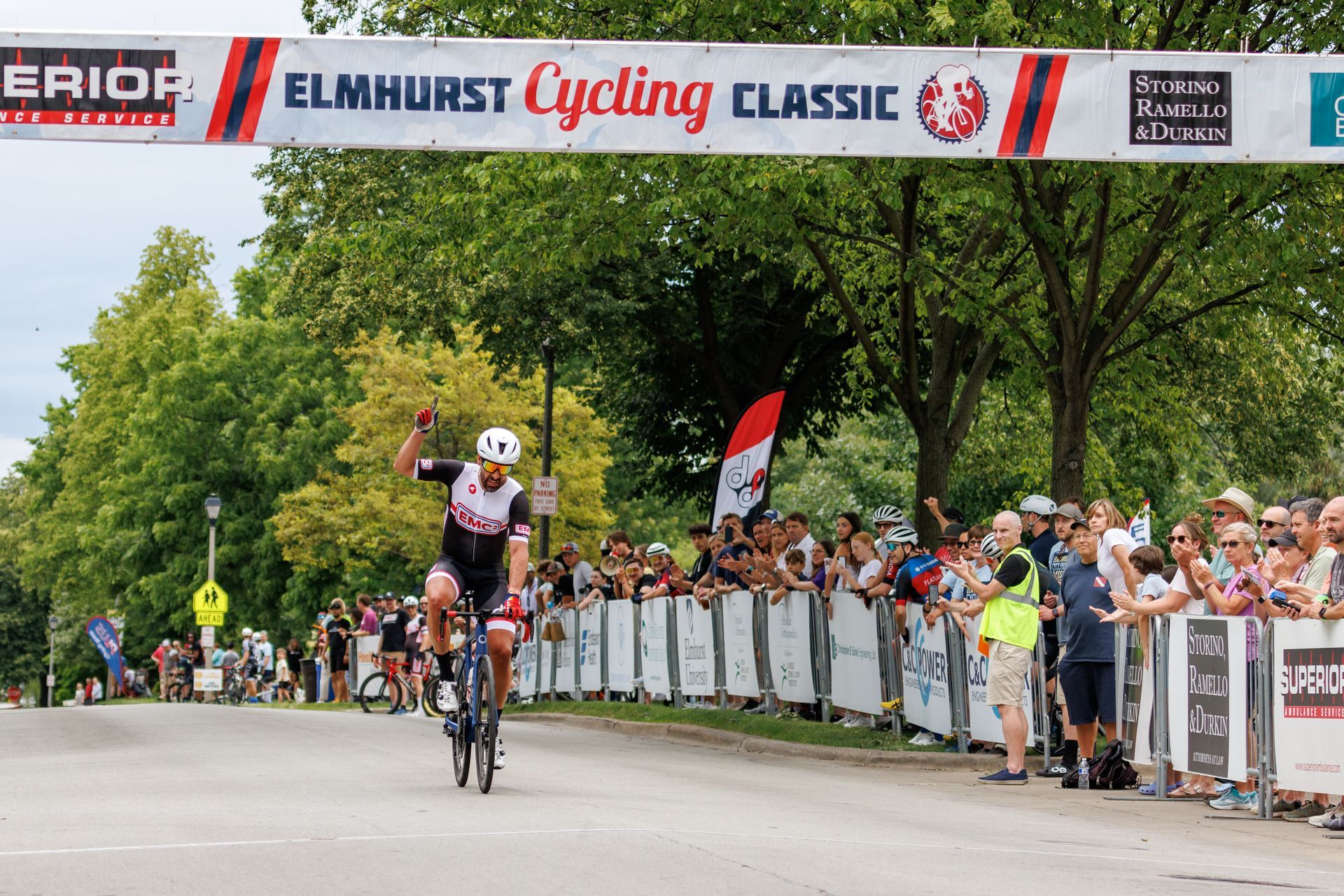 A man is riding a bike in front of a banner that says elmhurst cycling classic.