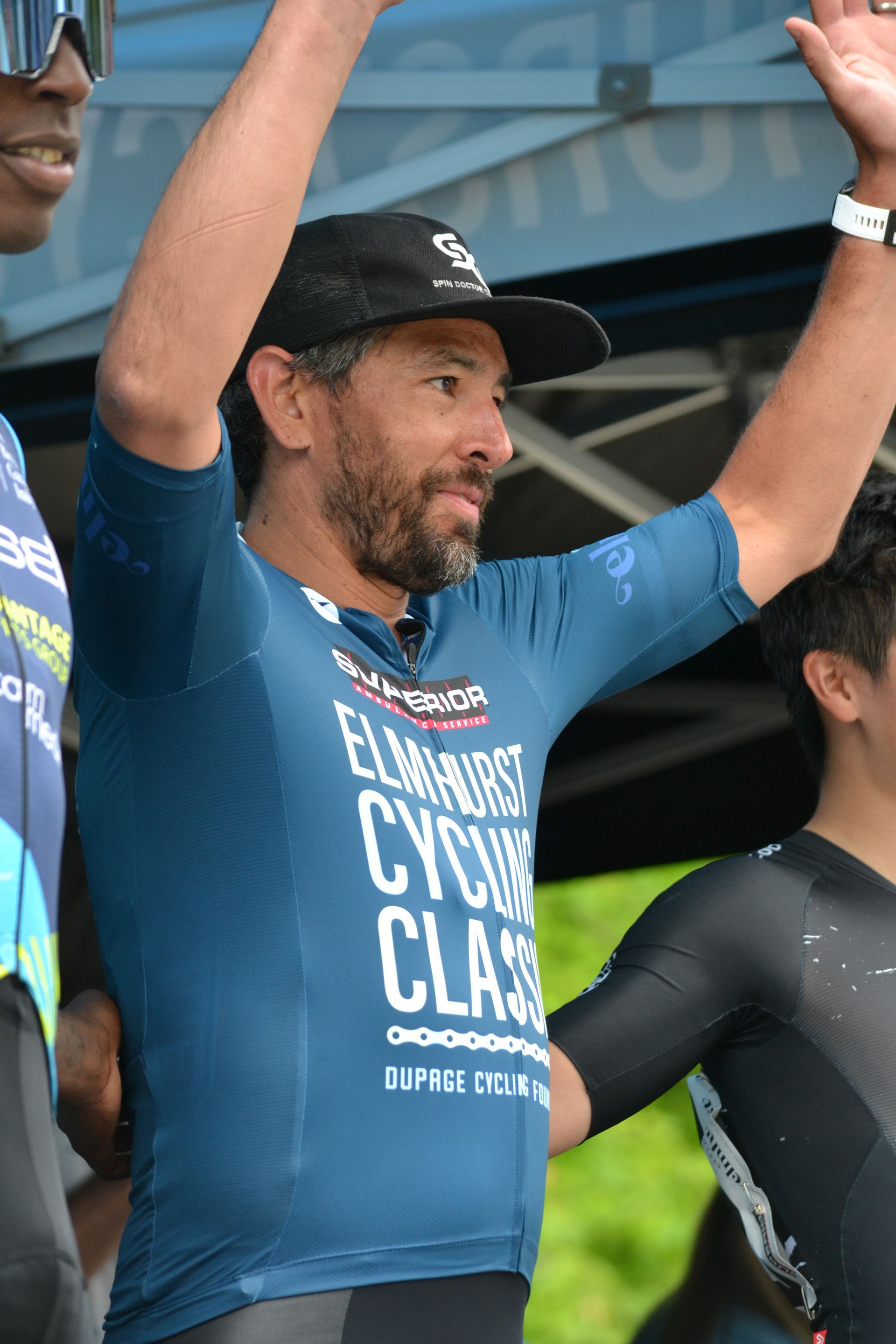 A man wearing a blue shirt that says cycling class is raising his arms in the air.