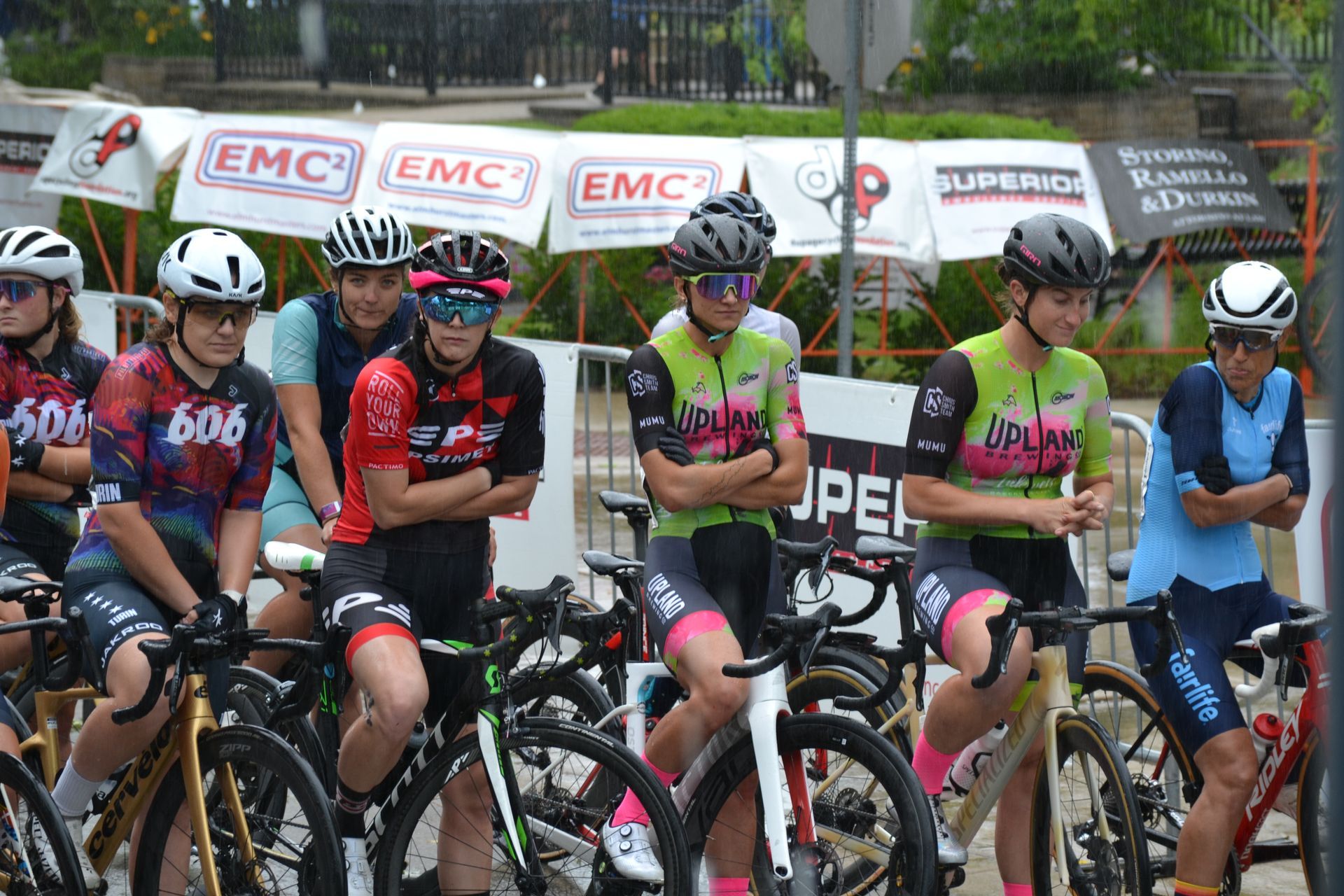 A group of cyclists are sitting on their bikes under an umbrella.