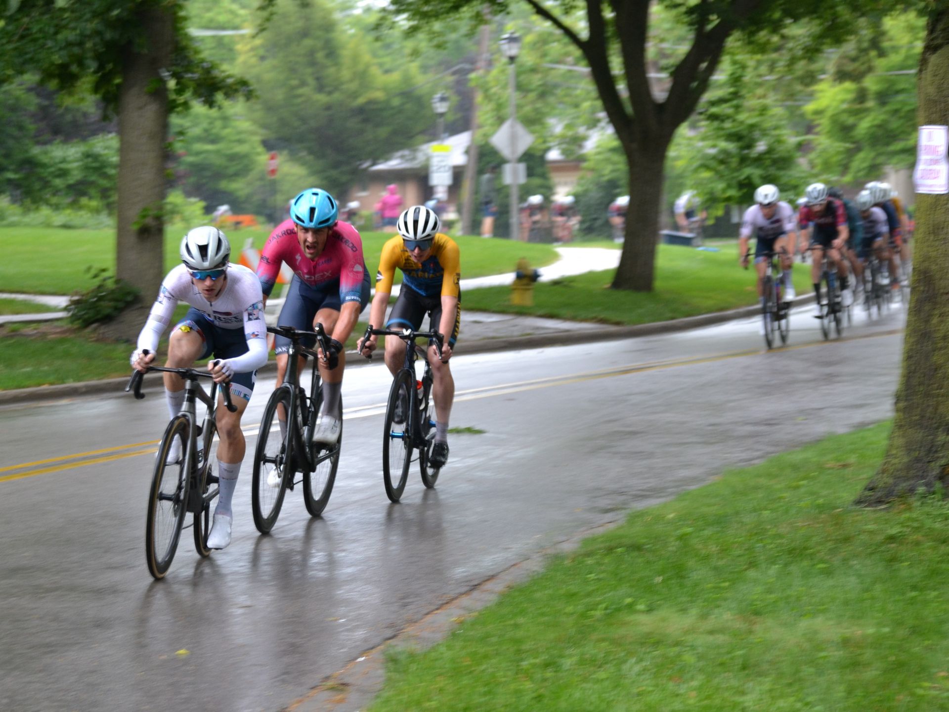 A group of cyclists are riding down a wet road